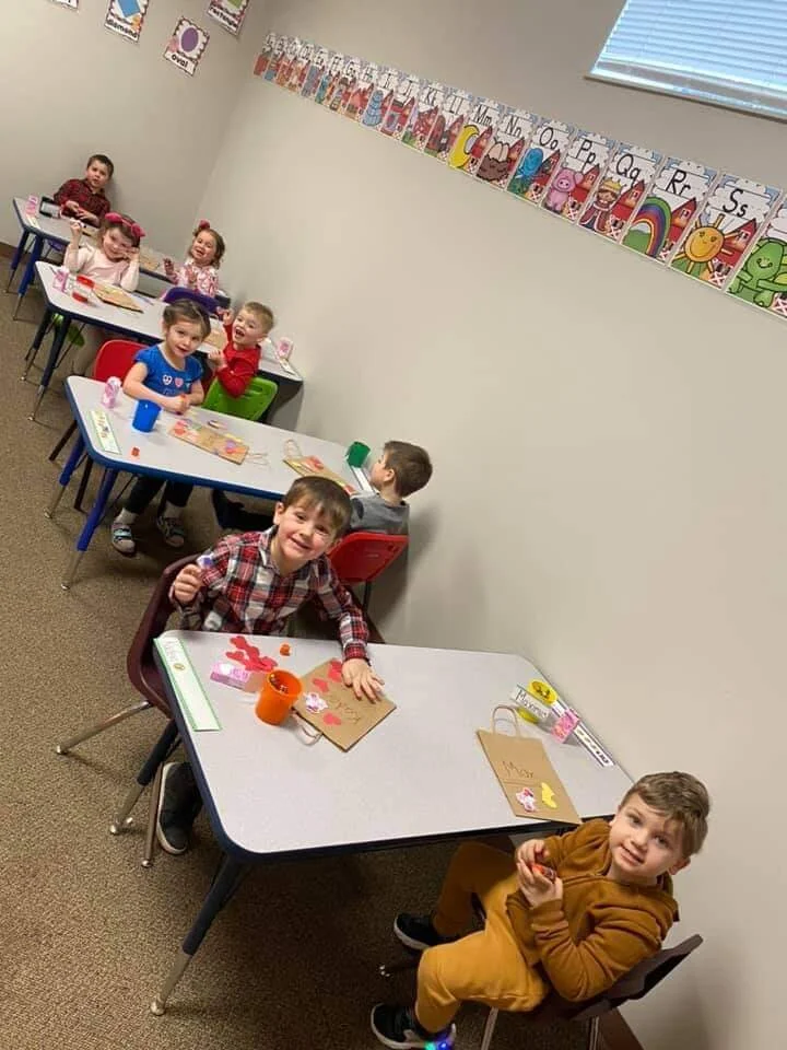 Six children sitting at desks in a classroom, engaging in arts and crafts activities.