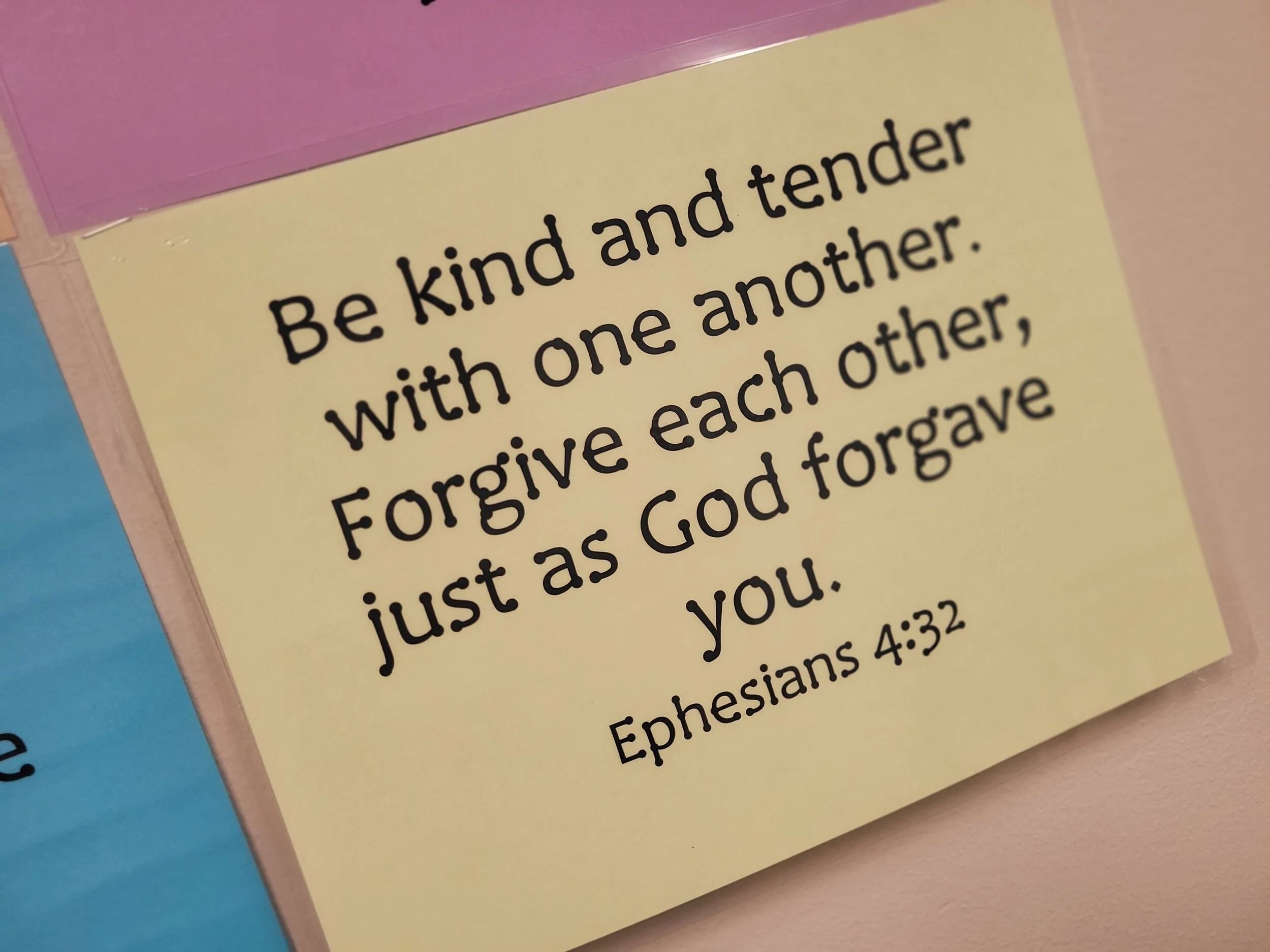 A printed quote on a yellow background reads, 'Be kind and tender with one another. Forgive each other, just as God forgave you.' The quote is attributed to Ephesians 4:32.