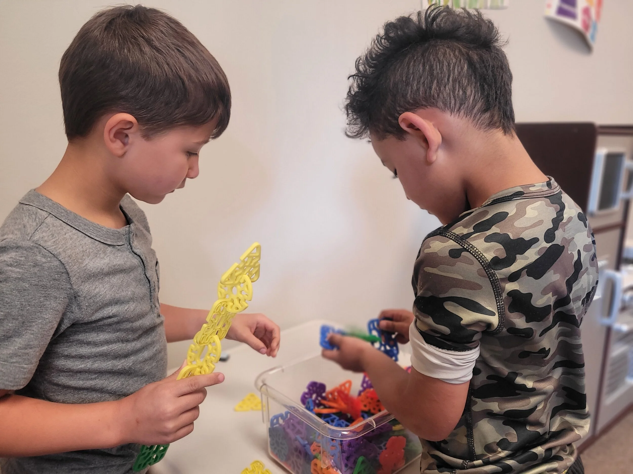Two young boys are playing with colorful plastic chain links in a kitchen setting.