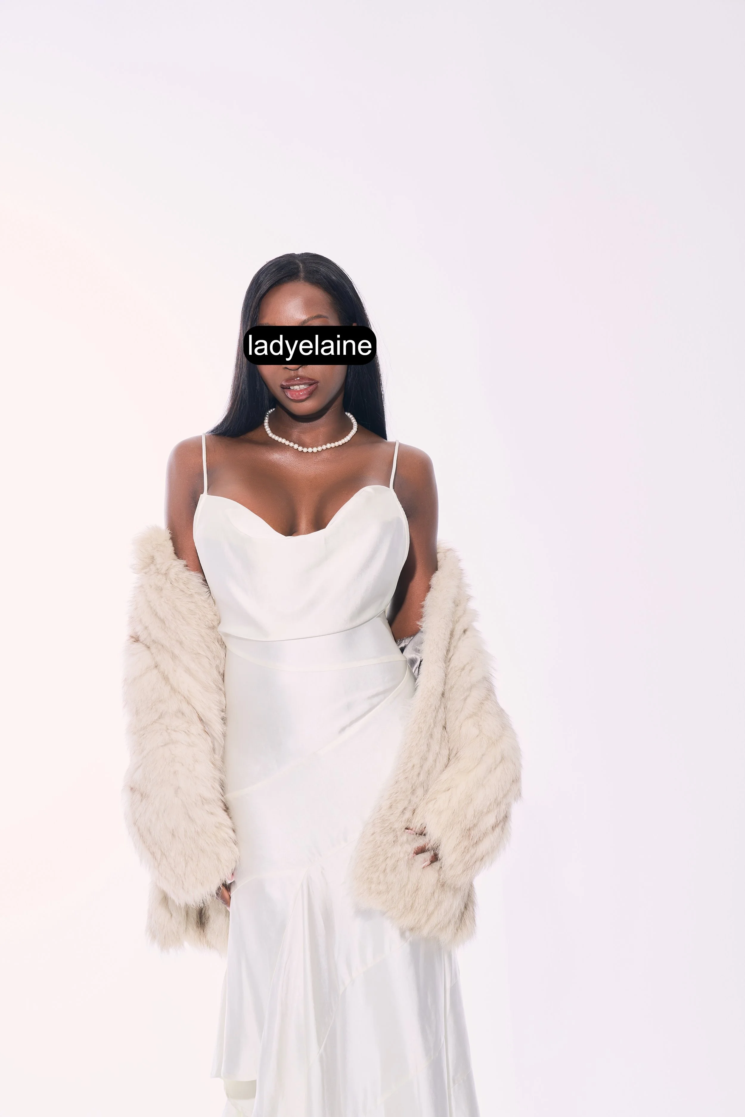 A woman in a white dress and fur coat with a pearl necklace, holding the coat. Her eyes are obscured with a black bar labeled 'ladyelane.'