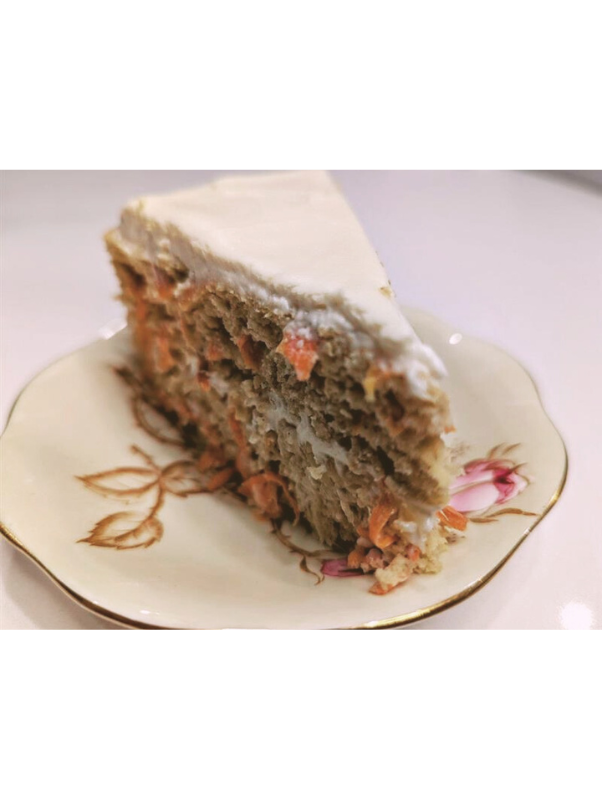 A slice of carrot cake with cream cheese frosting on a decorative floral plate.