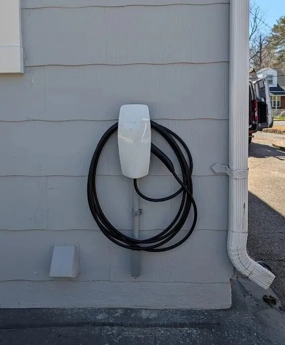 Electric vehicle charging station mounted on the exterior wall of a building, with black charging cables hanging from it.