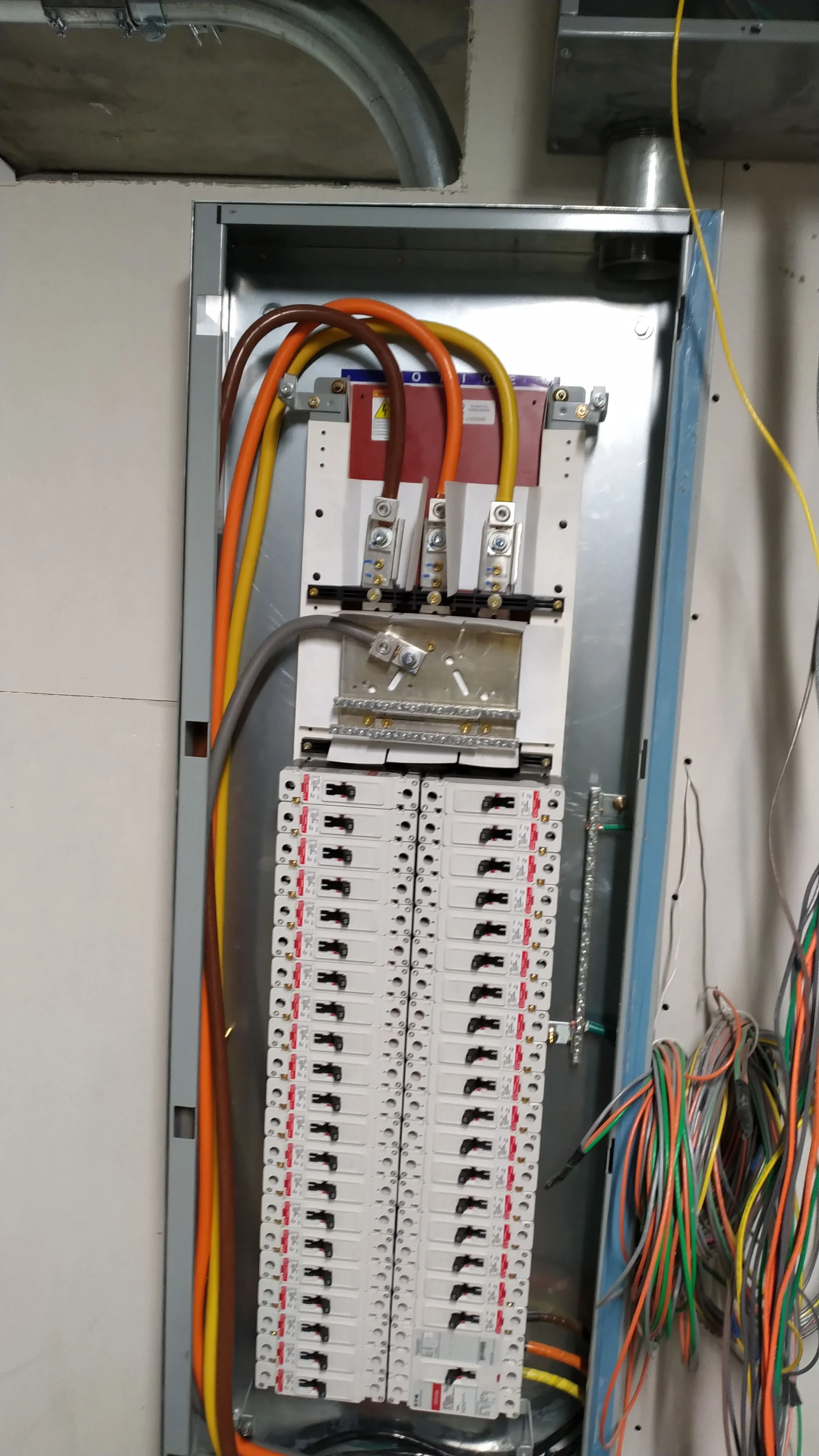 Electrical panel with circuit breakers, wiring, and electrical components inside a metal box, partially open.