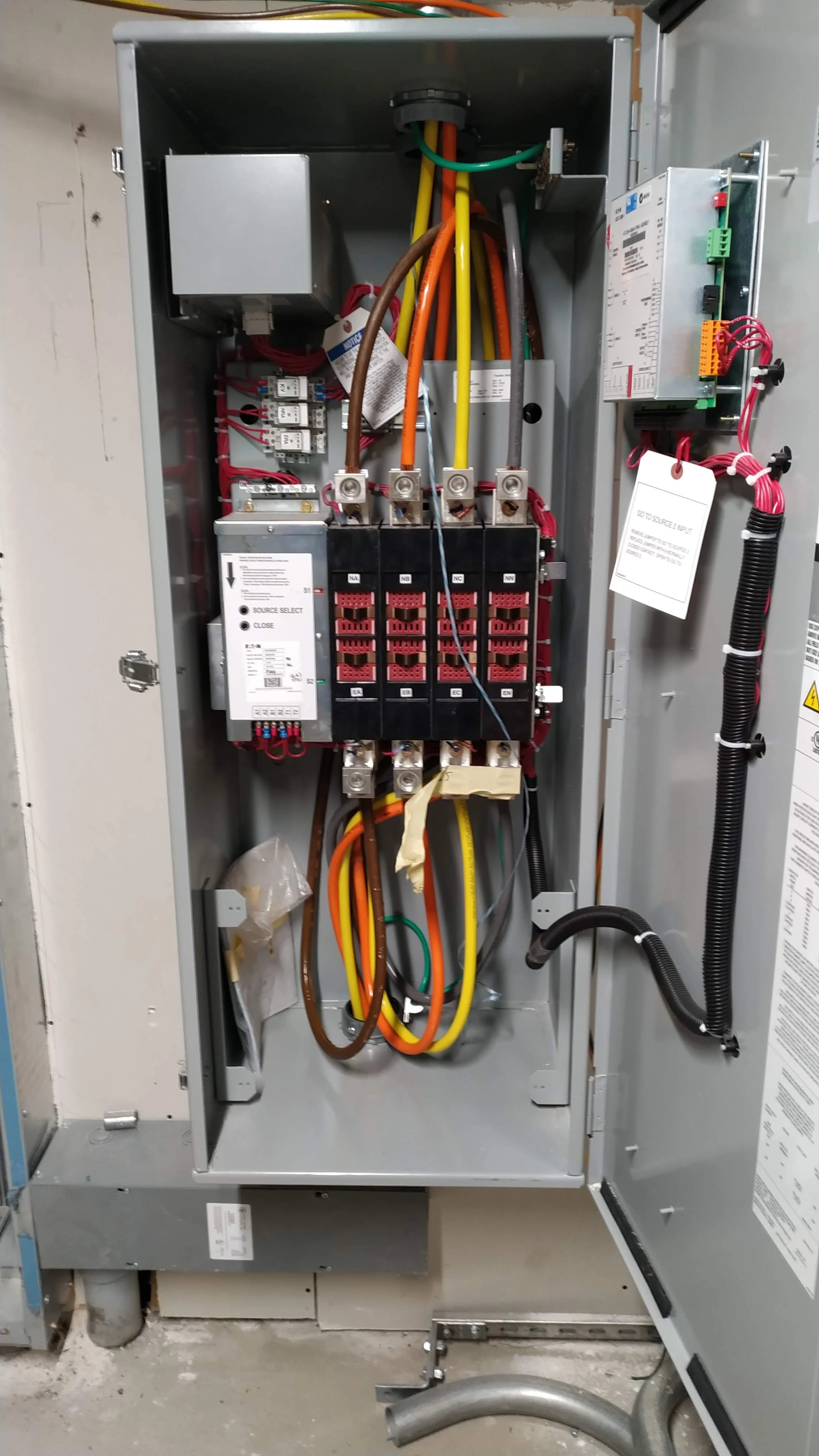 Open electrical control panel with various wires, circuit breakers, and electronic components inside.