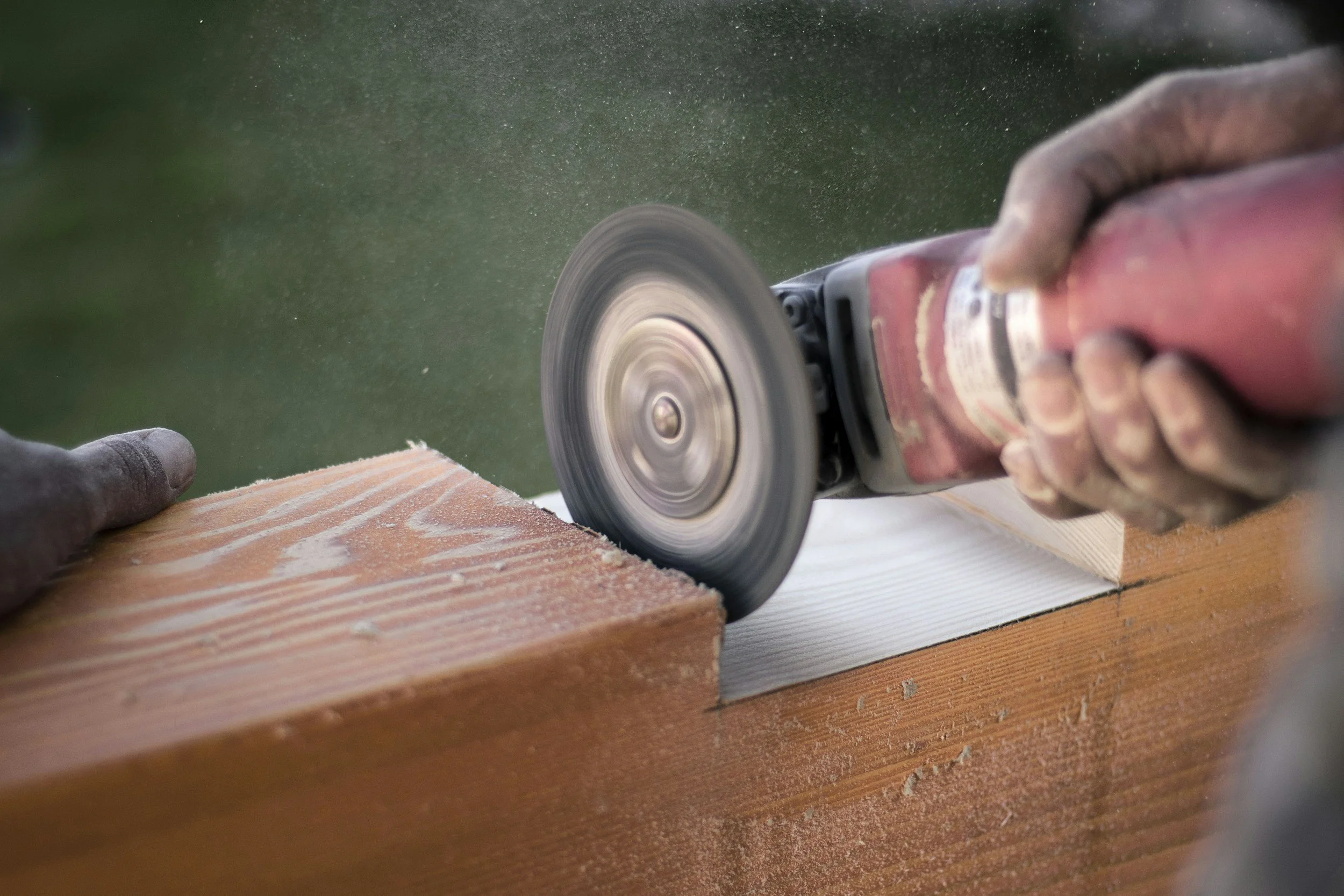 A person using an angle grinder to cut or smooth a piece of wood outdoors.