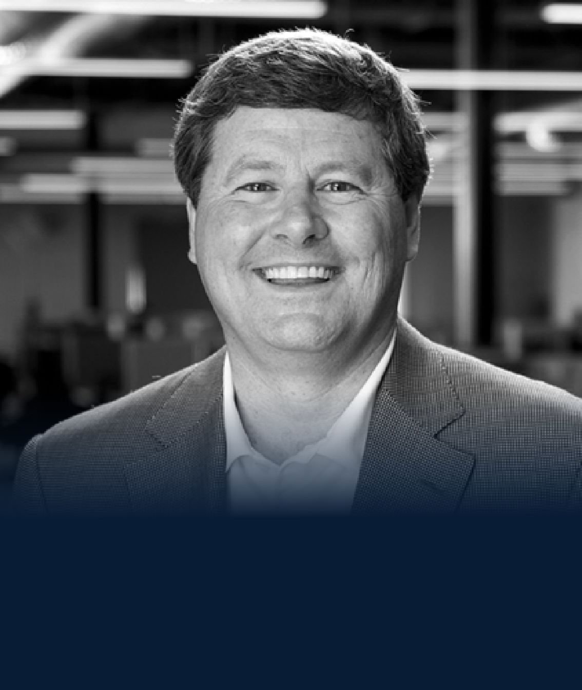 A smiling man in a suit, posed for a professional headshot, with a blurred background.