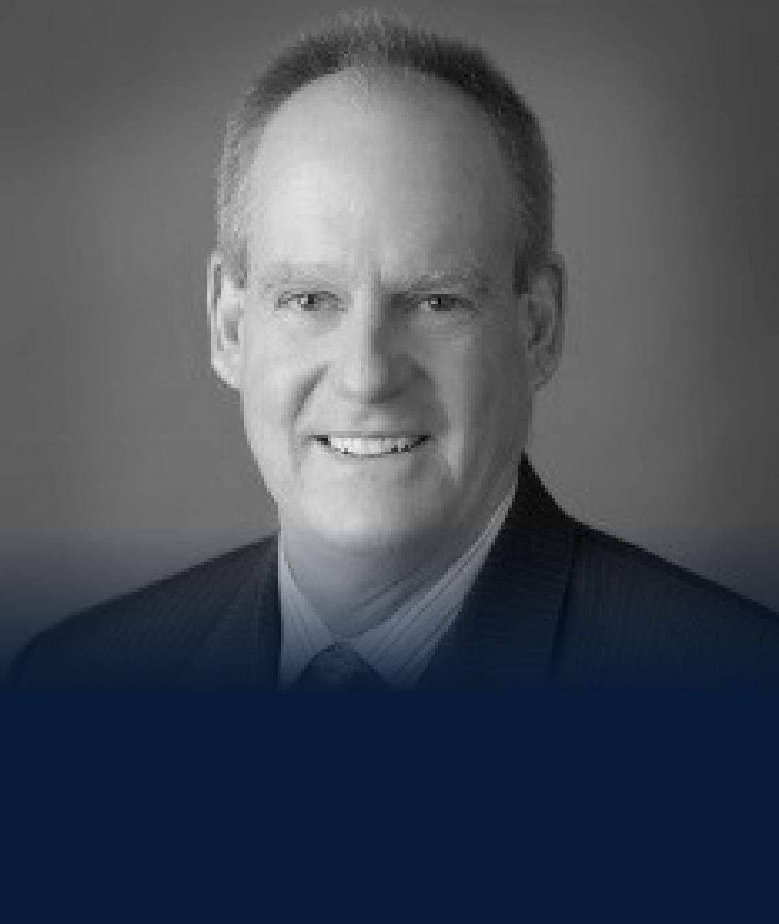 Black and white professional headshot of a smiling man in a suit and tie.