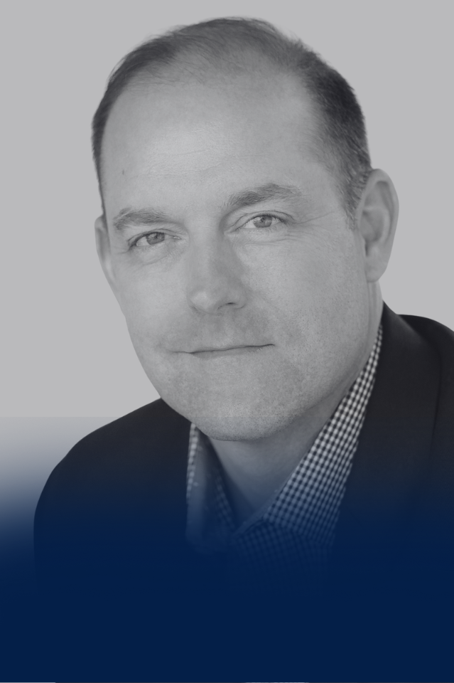 A black and white portrait of a man wearing a suit jacket and a checkered shirt, with a neutral background and gradient overlay.