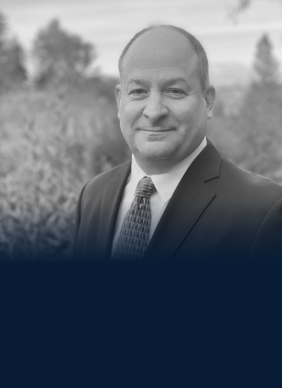 Black and white portrait of a middle-aged man wearing a suit and tie, outdoors with a blurred natural background.