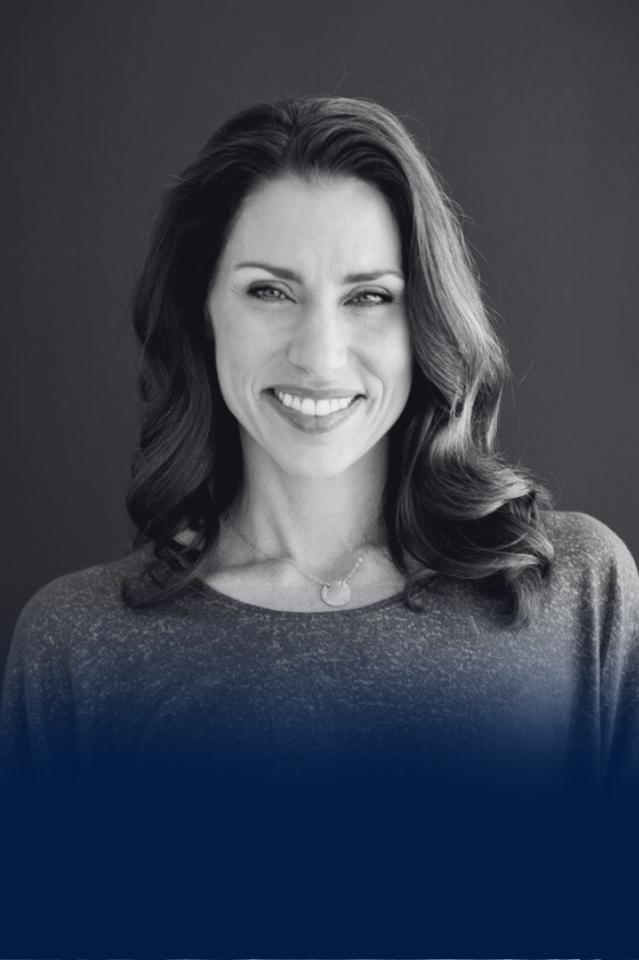 Black and white portrait of a smiling woman with wavy hair wearing a top and a necklace.