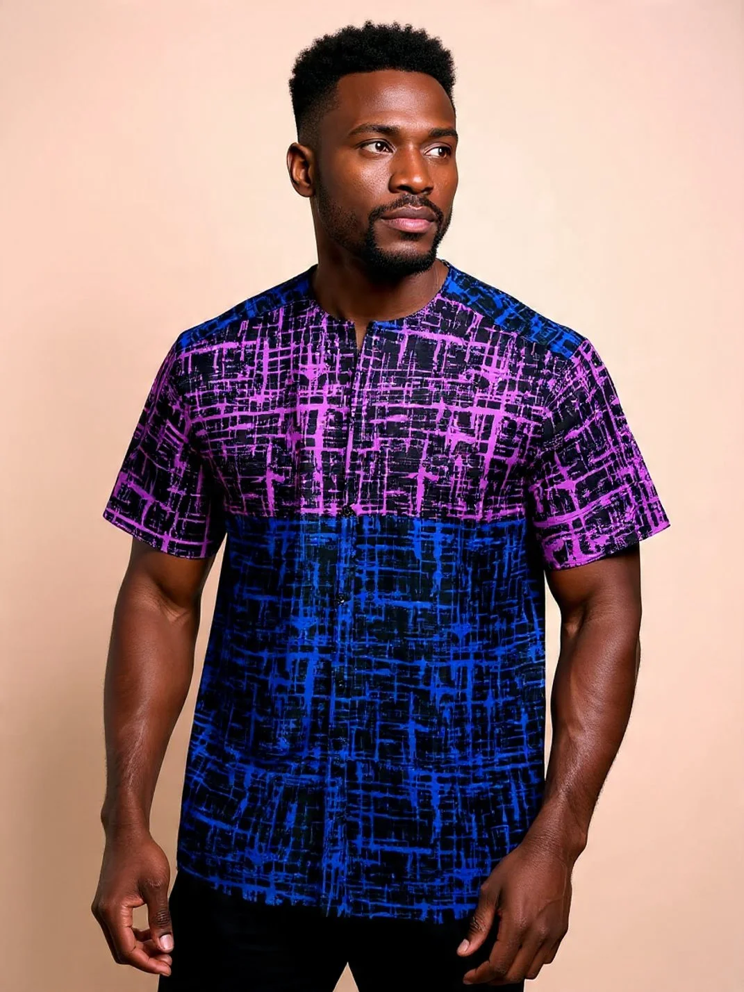 A man with dark skin and short curly hair wearing a colorful shirt with purple, pink, and blue abstract patterns, standing against a plain beige background.