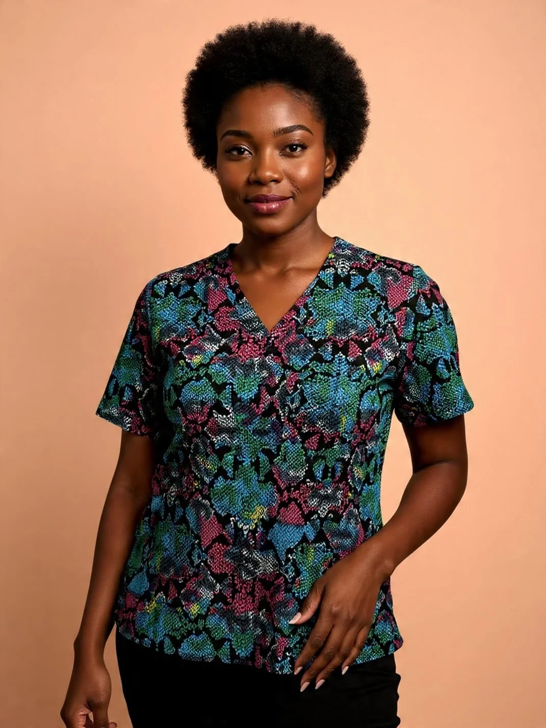 Portrait of a woman with short curly hair wearing a colorful patterned top against a peach-colored background.
