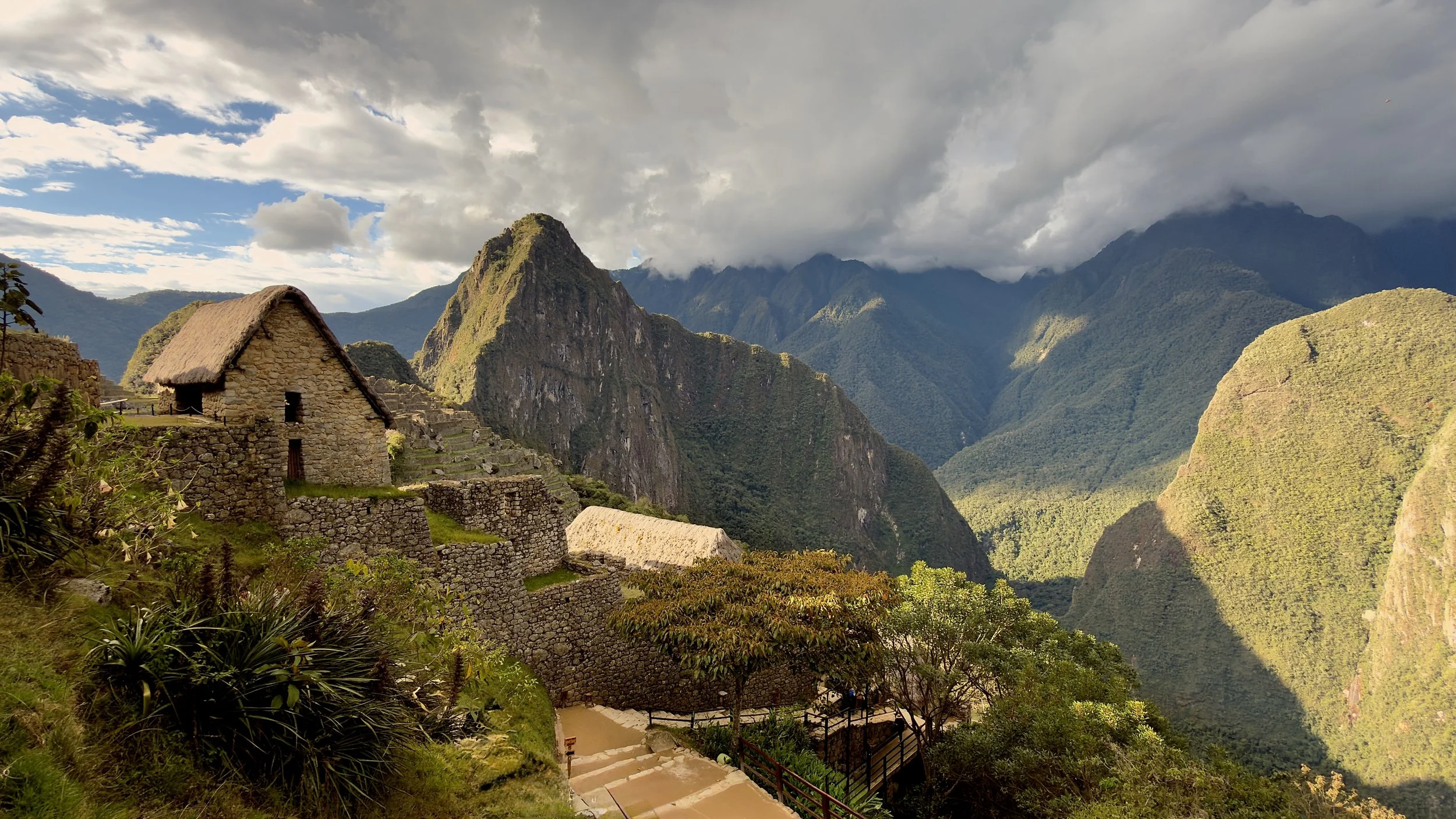 Ancient stone buildings and terraces at Machu Picchu surrounded by steep, green Andean mountains under a partly cloudy sky