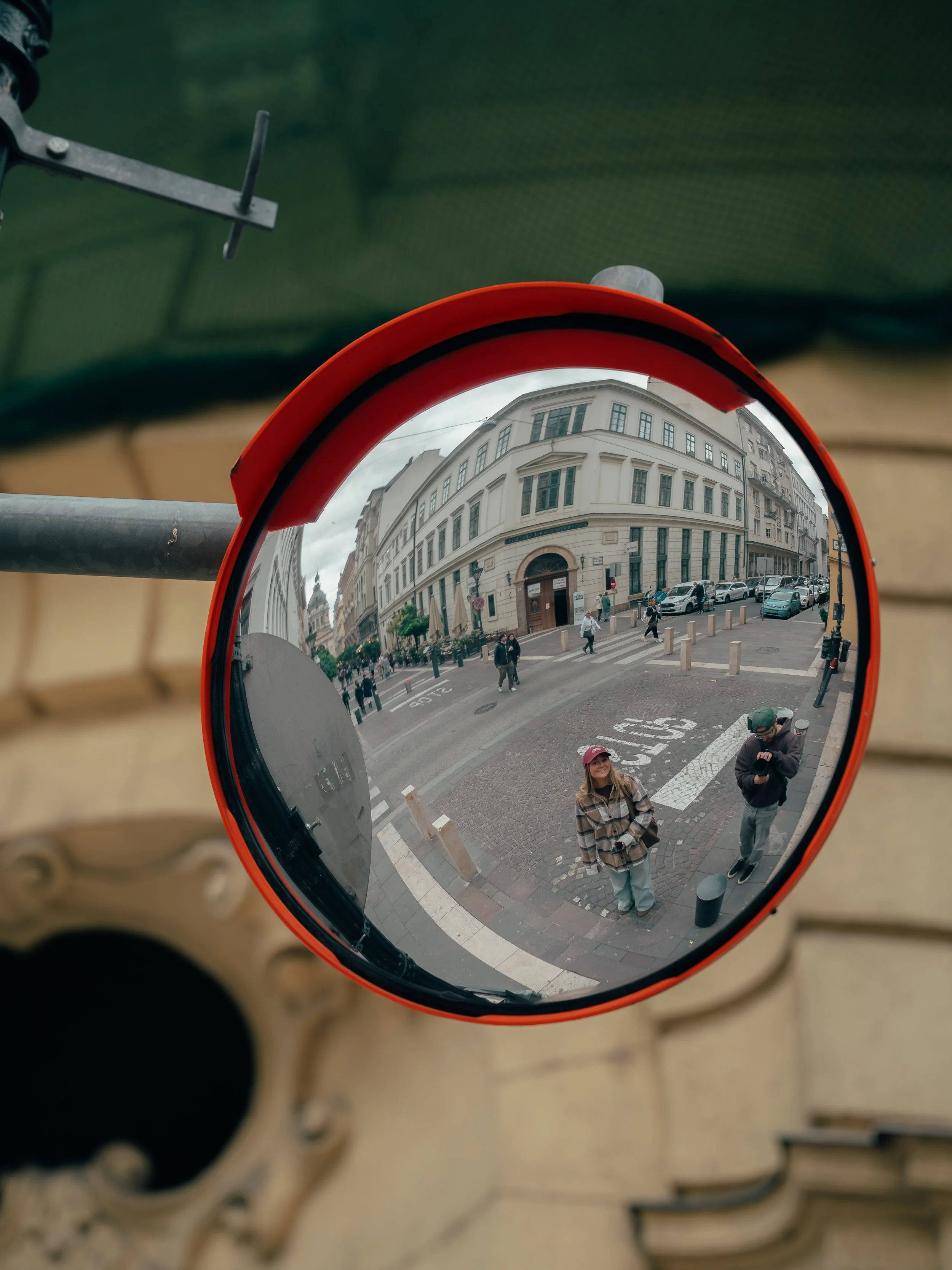Reflected city street scene in a convex mirror showing pedestrians, vehicles, and historic buildings