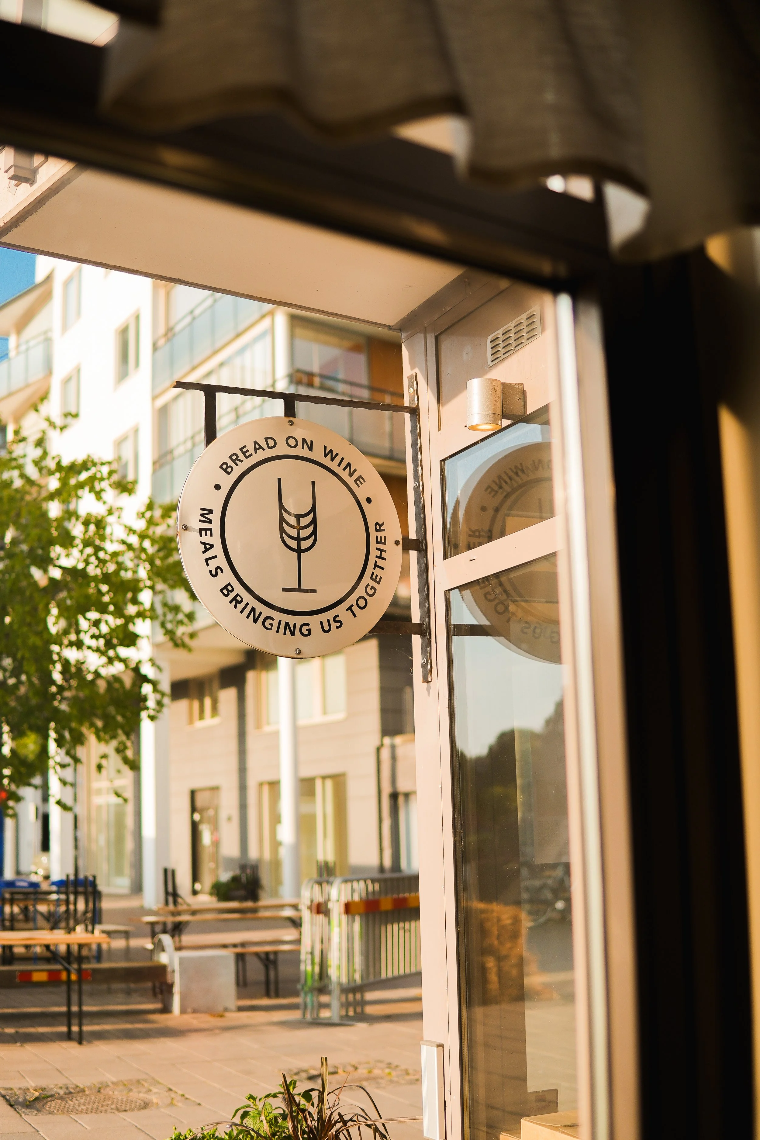 Sign outside a restaurant with a wheat symbol and the text "Bread on Wine, Meals Bringing Us Together."