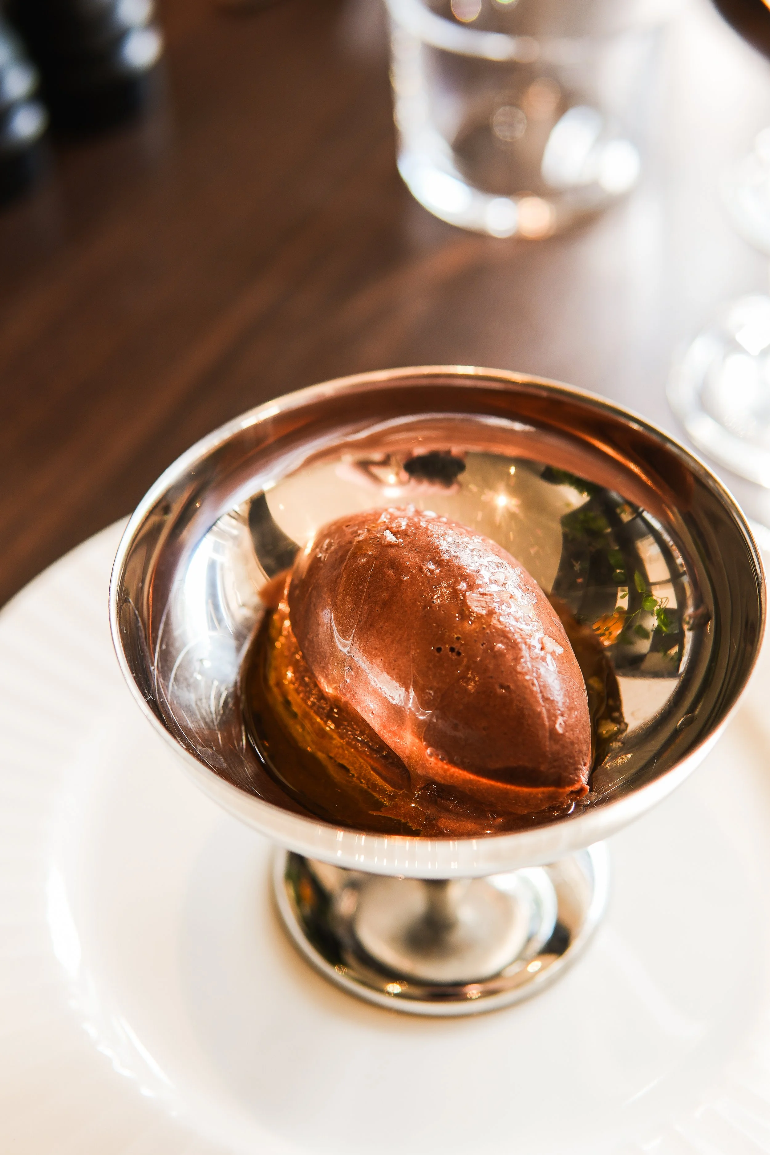A scoop of chocolate ice cream in a silver dessert cup on a white plate.