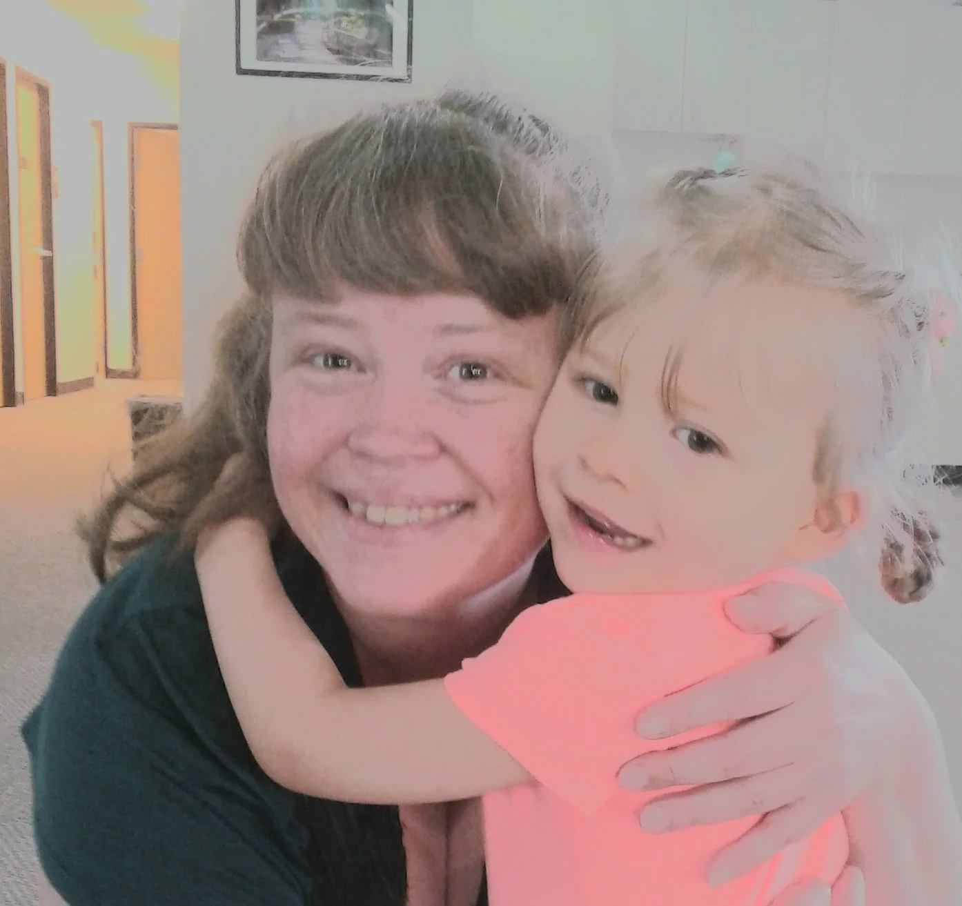 A picture of a woman and a young girl hugging and smiling. They both look happy and are close to each other.