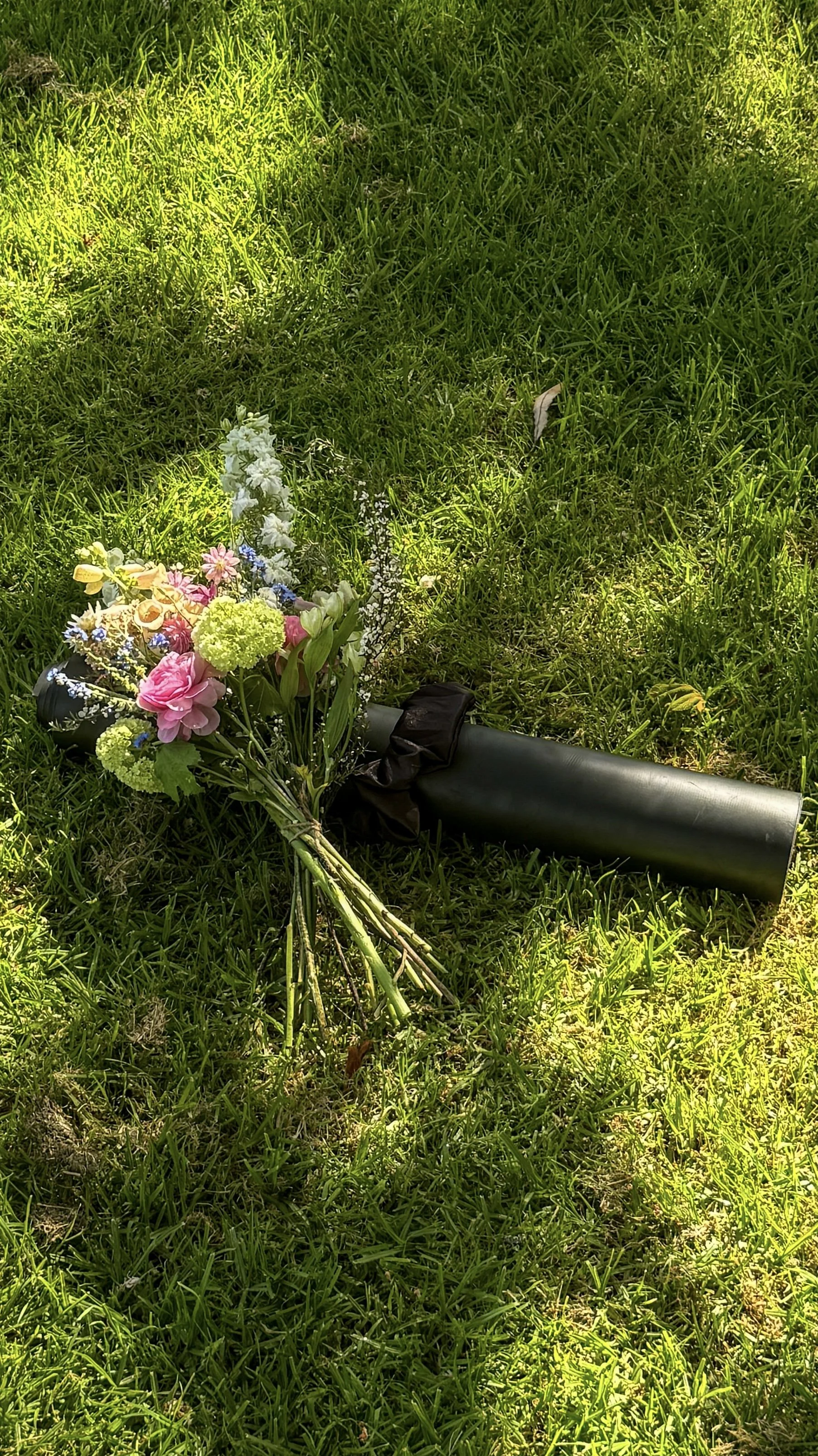 Bouquet of colorful flowers with a black umbrella lying on green grass, in sunlight.