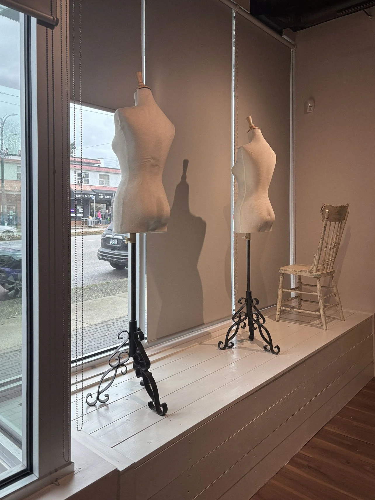 Two dress forms on stands and a wooden chair displayed in a store window.