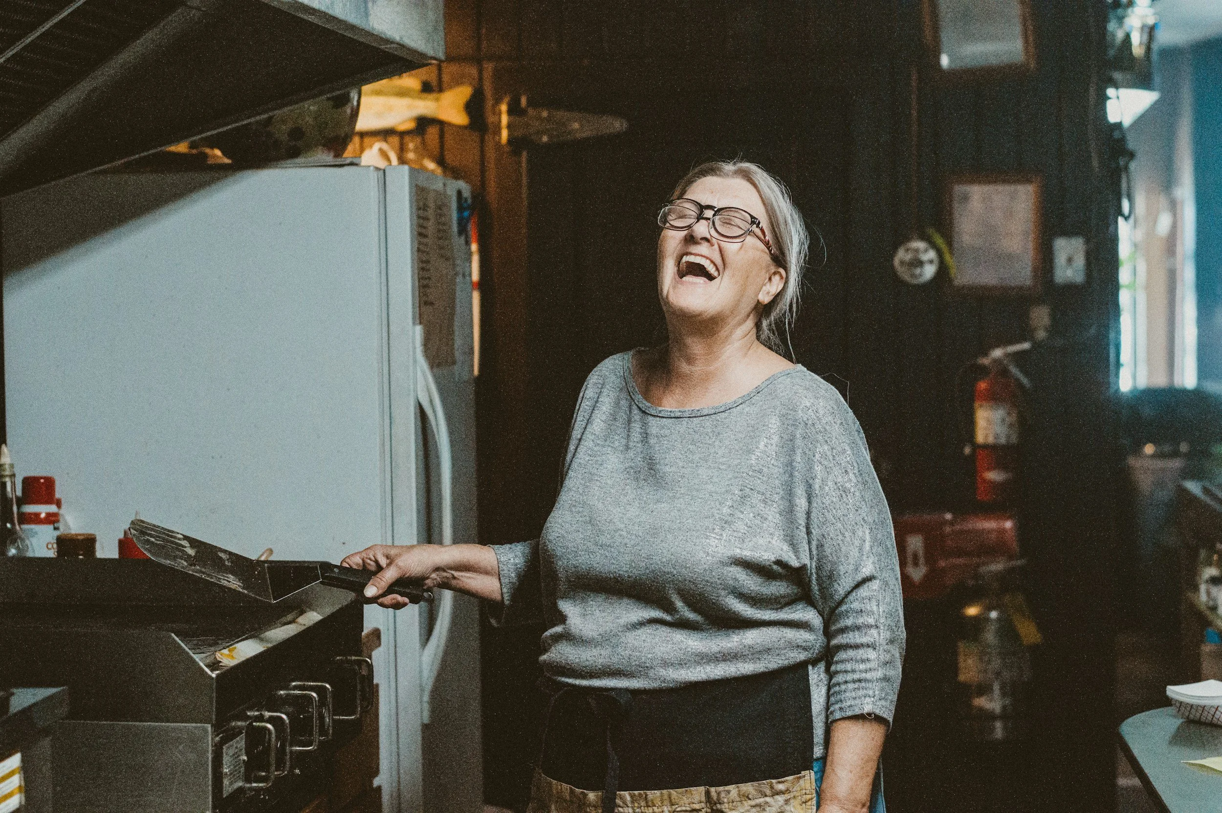 A woman laughing and cooking on a stove in a kitchen.