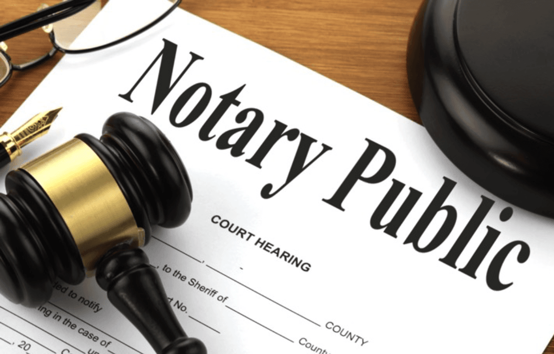 Notary Public paperwork with a black and gold gavel, a gold pen, and glasses on a wooden surface.