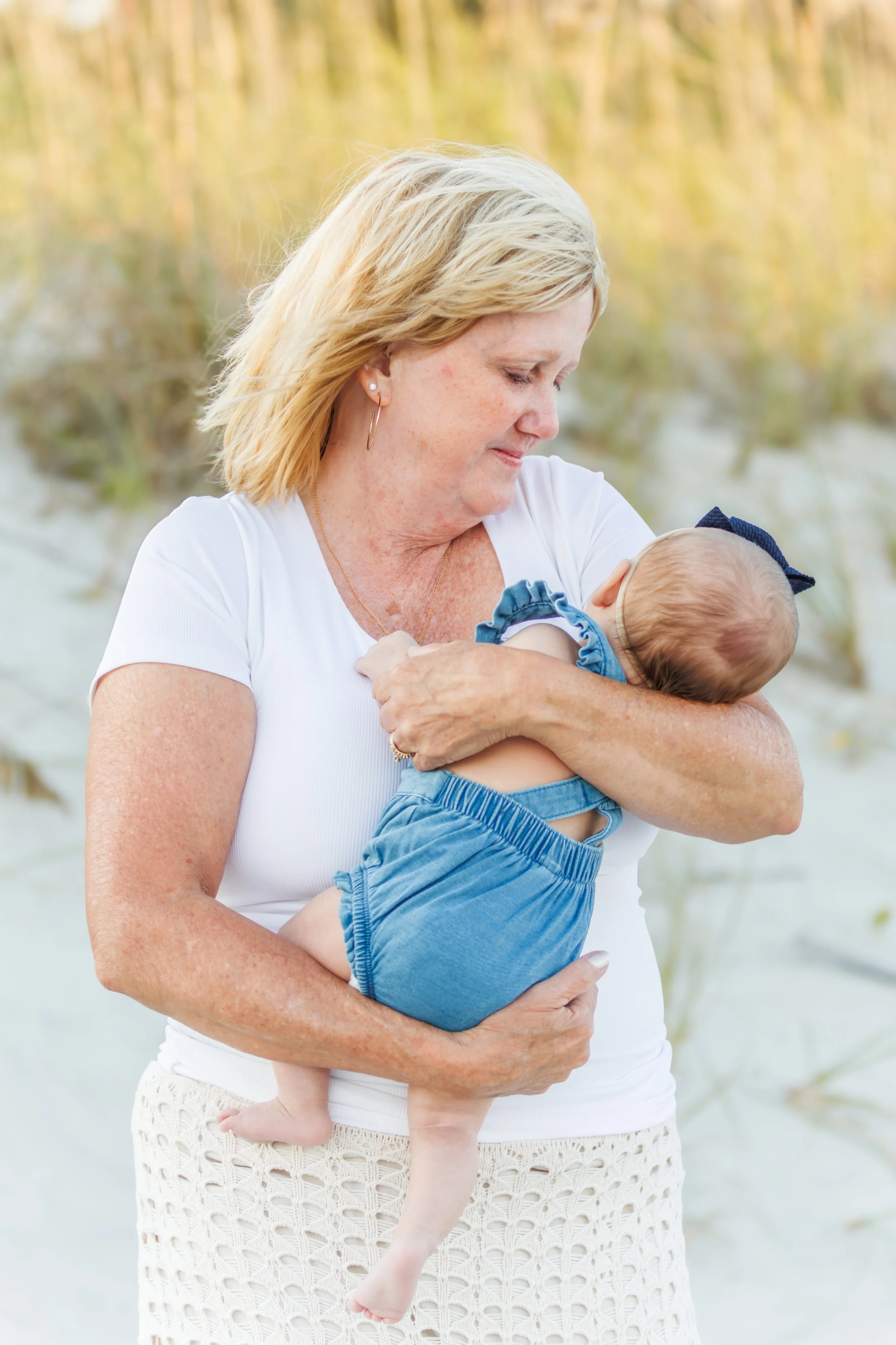 A woman holding a baby in an outdoor setting with grass and trees in the background.
