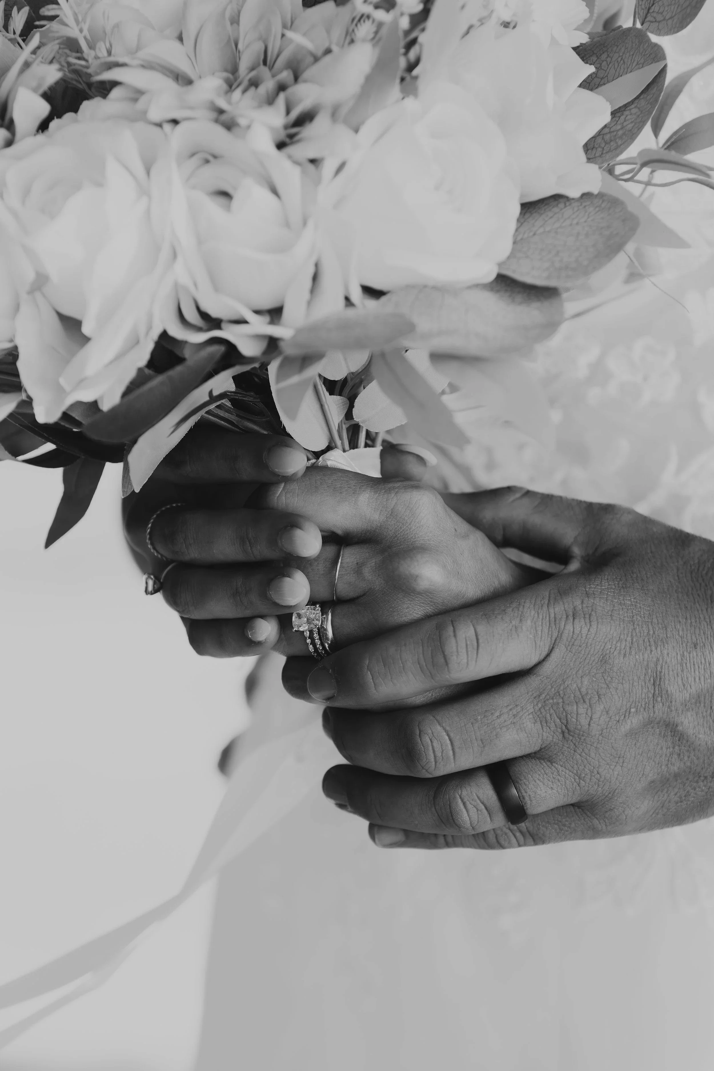Close-up of hands with wedding rings holding a bouquet of flowers in black and white.