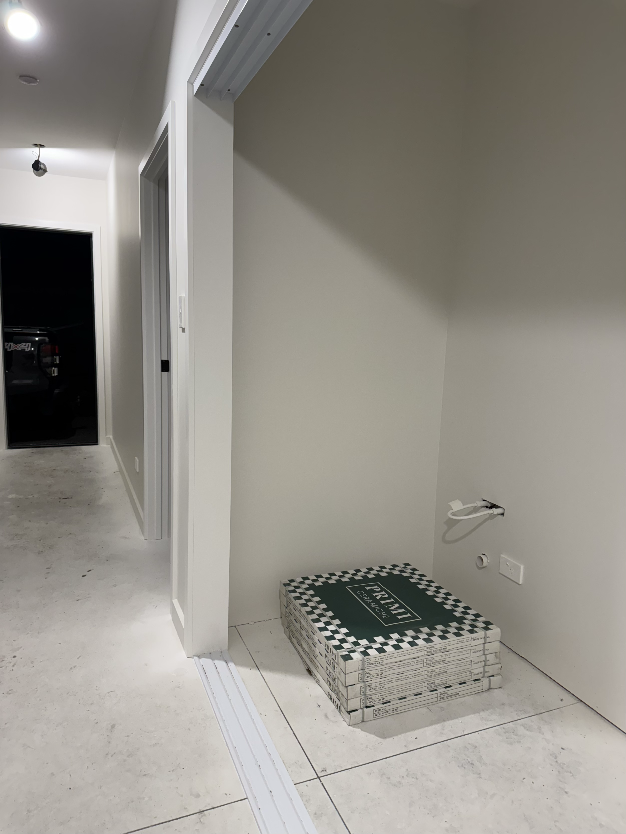 Stacked boxes of Primo ceramic tile in a room under construction, with wall outlets and plumbing visible.