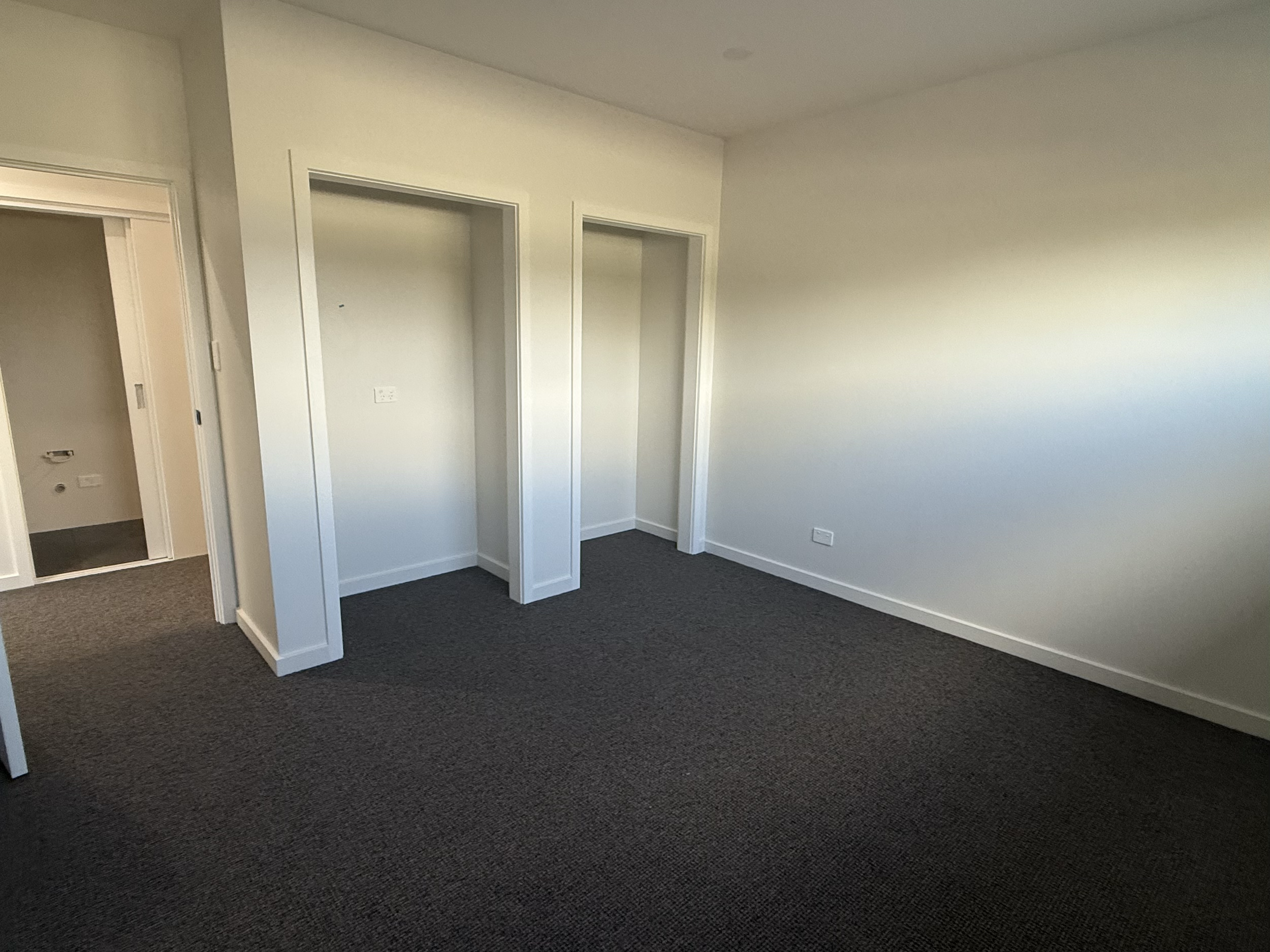 Empty room with white walls, dark carpet, and two empty closet spaces.