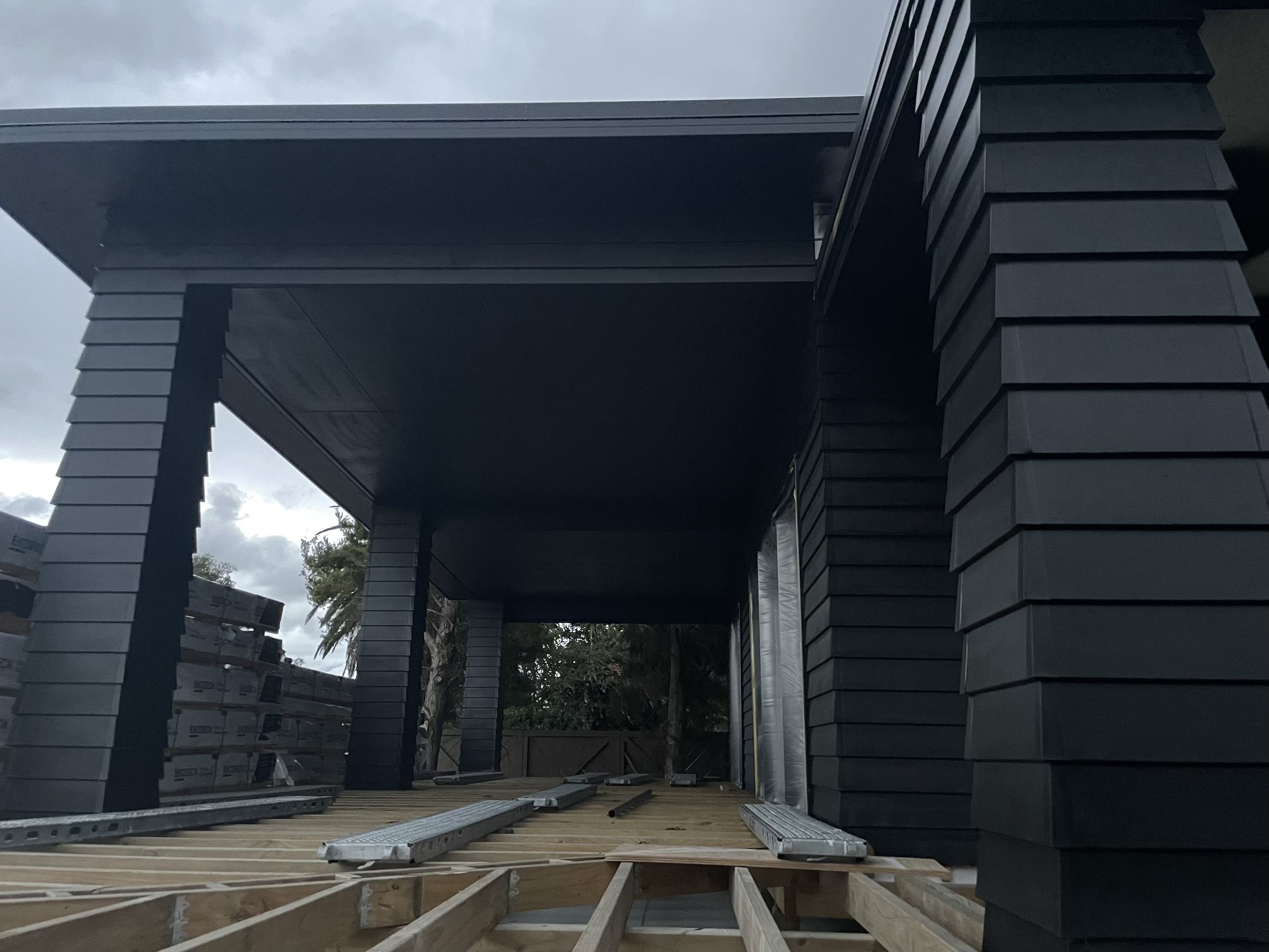 Under construction black building with wooden deck and metal ladders.