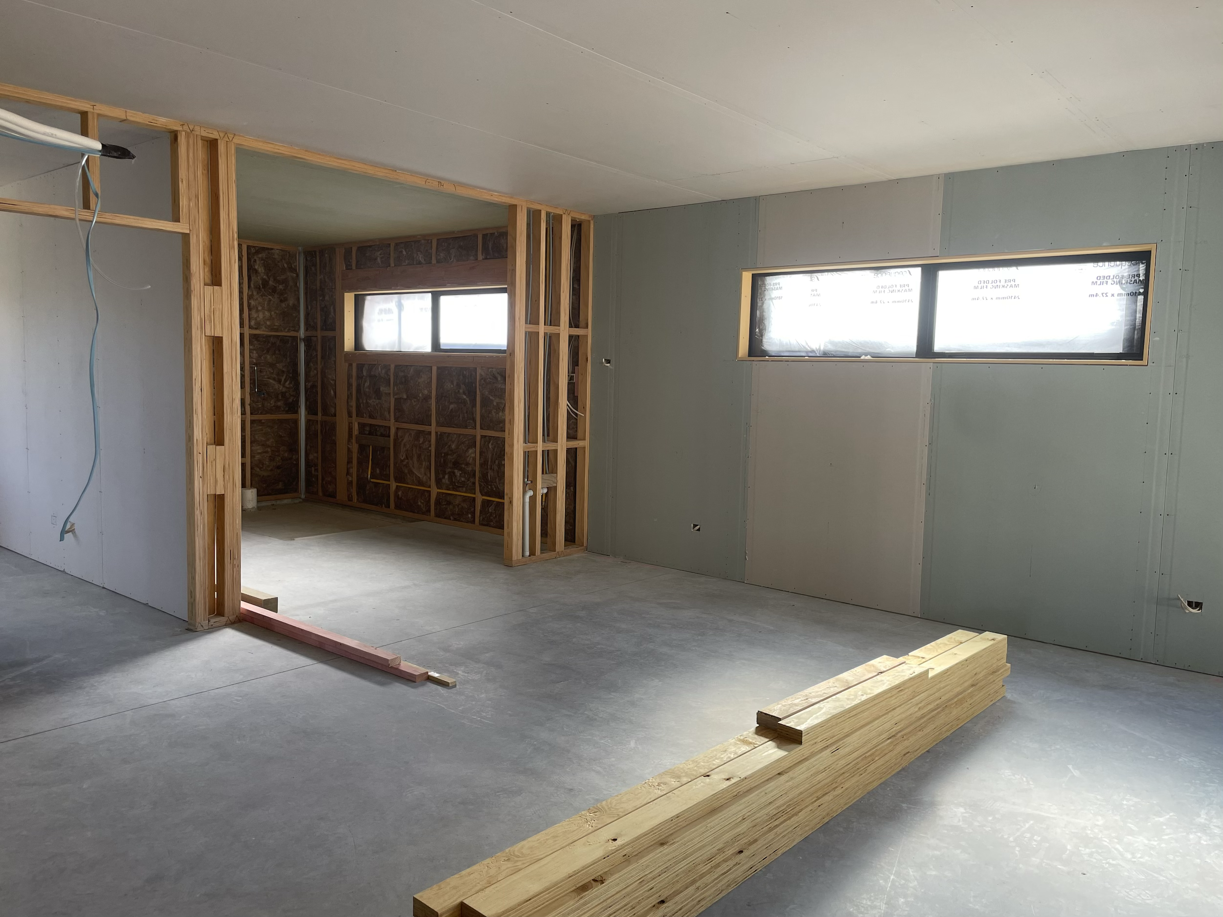 Interior view of a room under construction with unfinished drywall and wooden framing, and a window with partial daylight.
