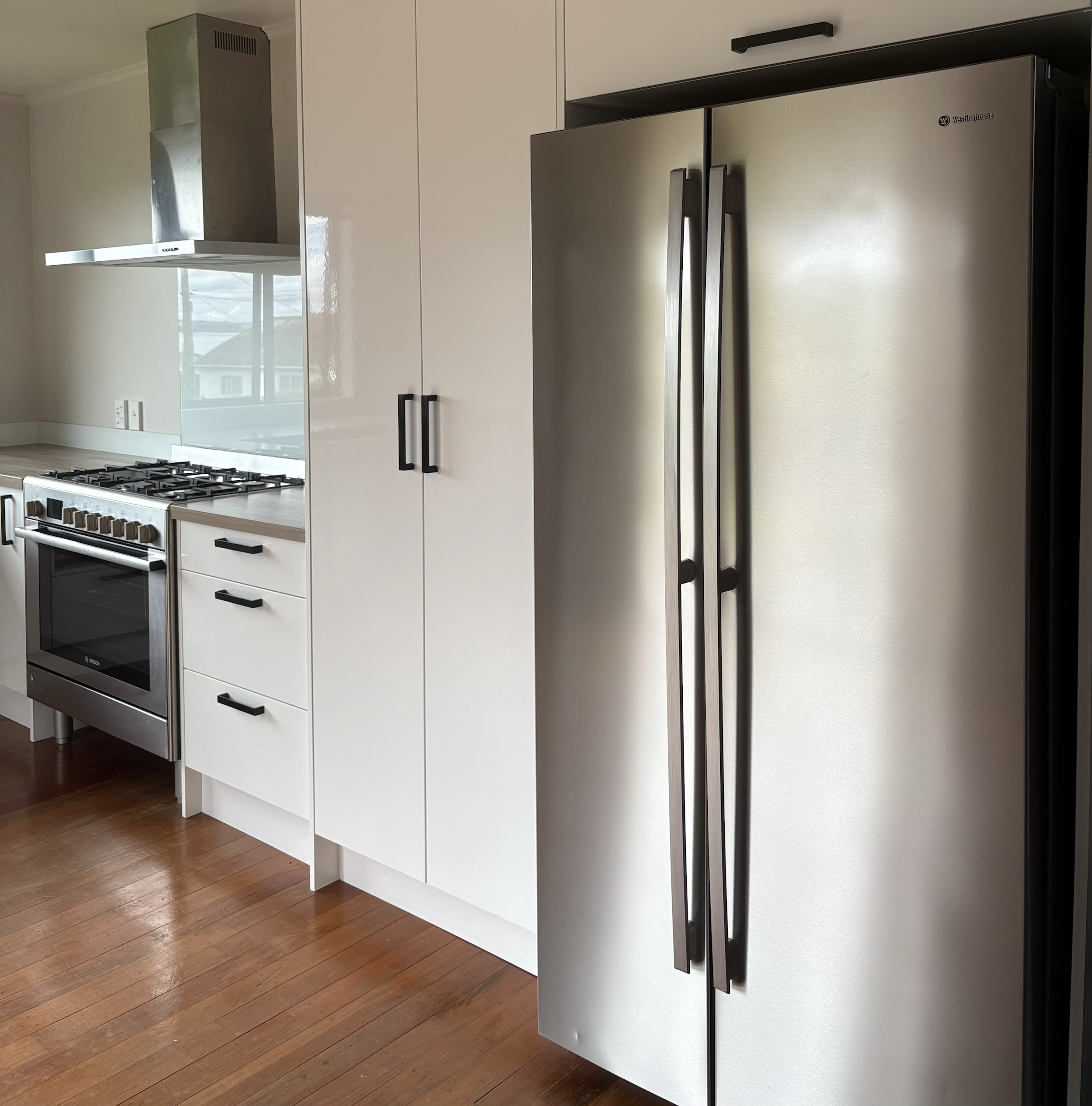 Modern kitchen with white cabinets, a stainless steel refrigerator with black handles, a gas stove, and wooden flooring.