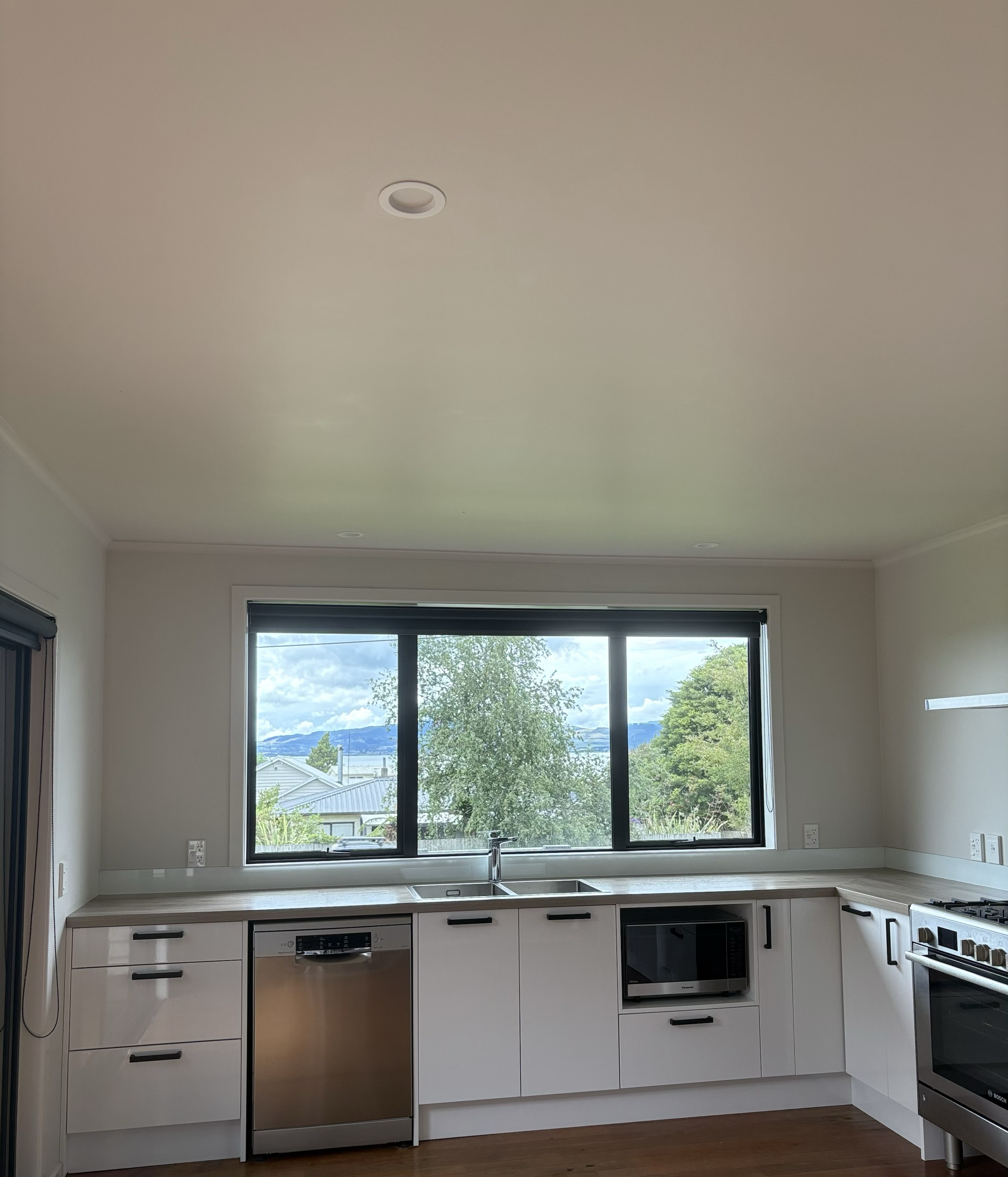 Kitchen with white cabinets, modern appliances, large window showing trees and mountains outside.