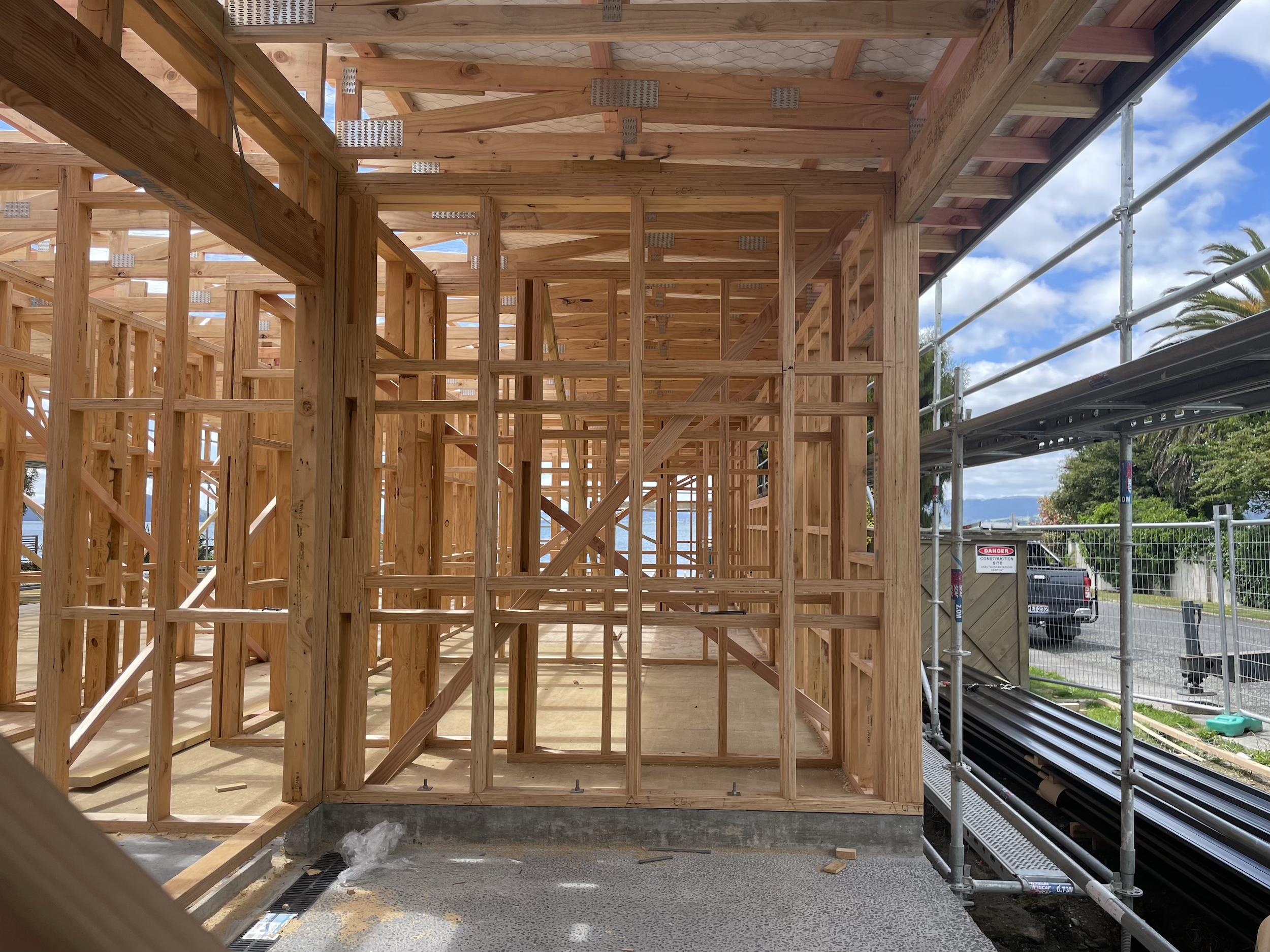 Wooden framework of a building under construction, with scaffolding and partially completed roof, outdoors on a sunny day.