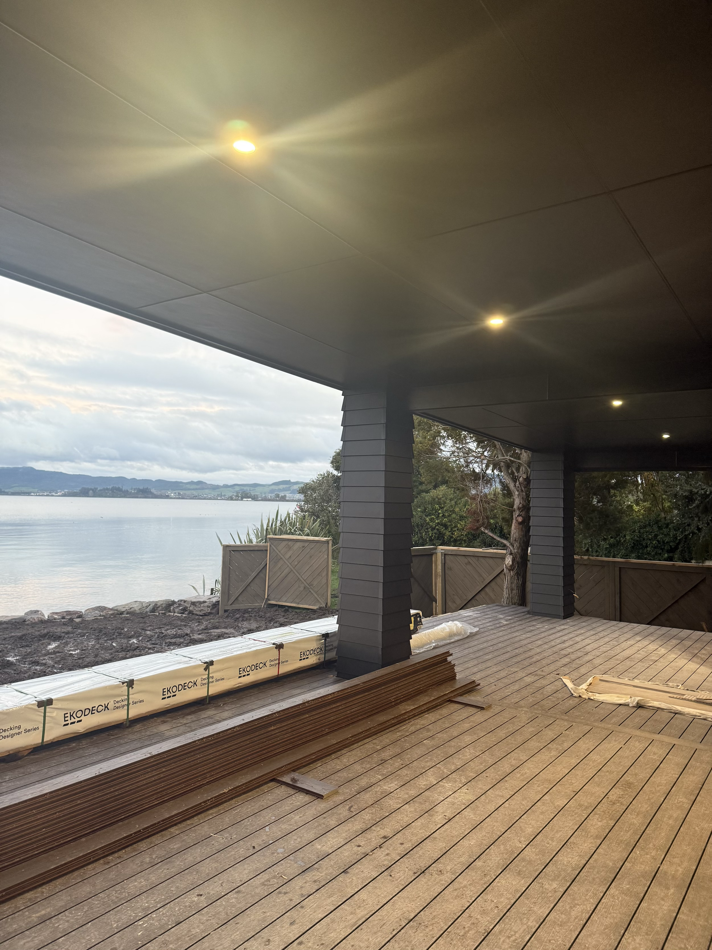 Construction area of a deck by a water body, with black painted columns, wooden planks, and some construction materials.