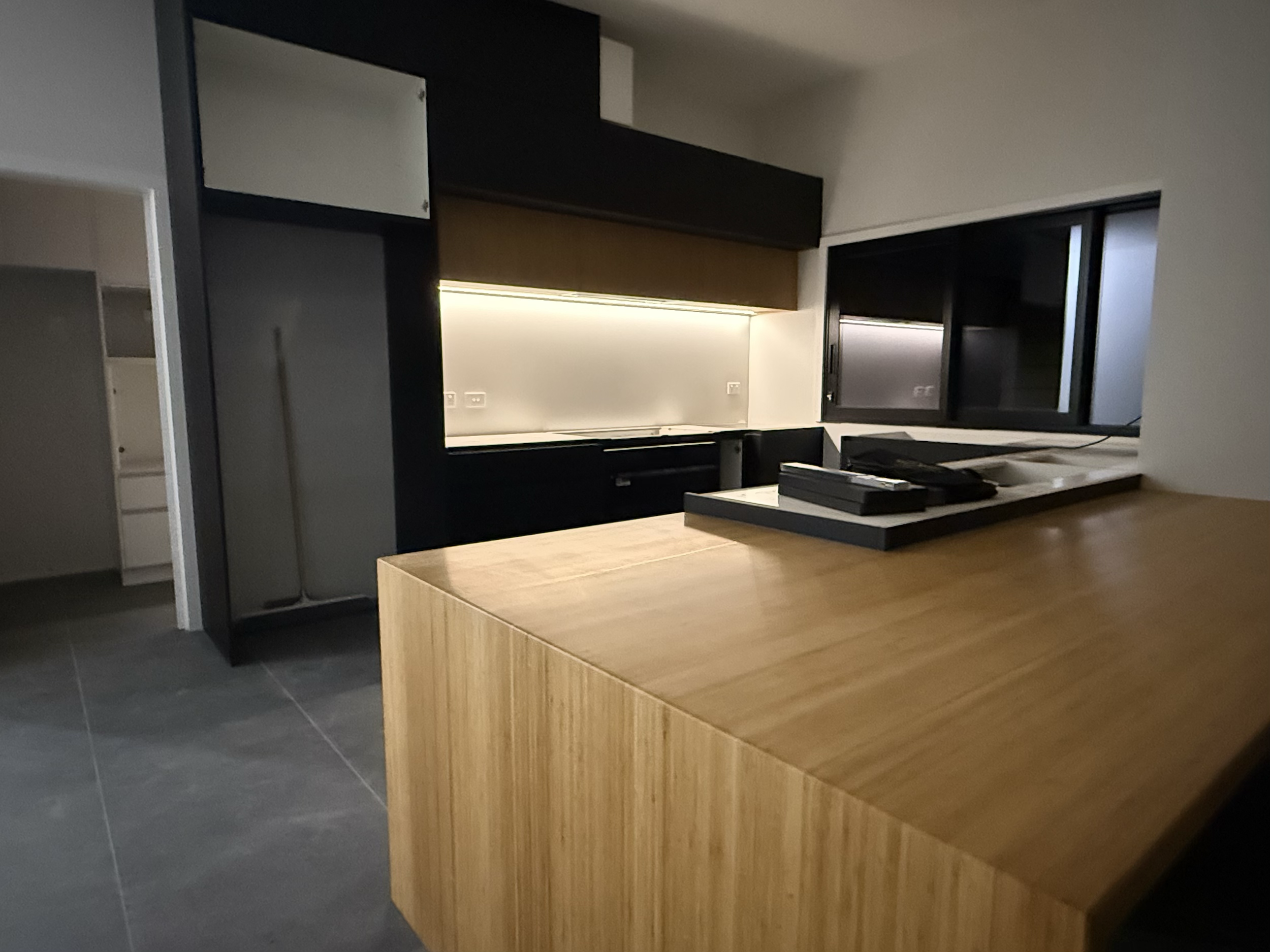 Modern kitchen with wooden island, black cabinets, a backsplash with under-cabinet lighting, and a window with sliding glass panes.