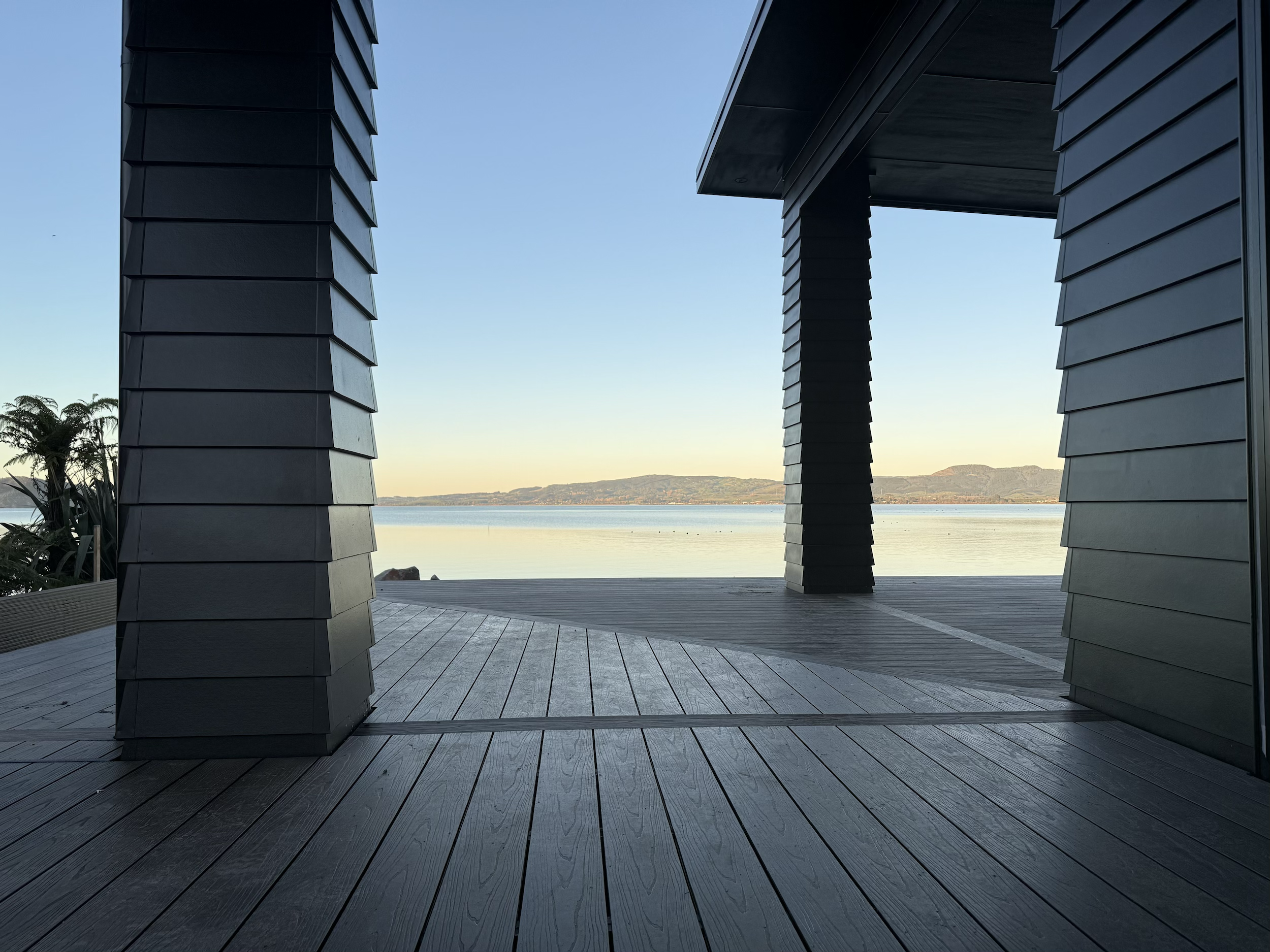View of calm water and distant hills through a covered outdoor space with black architectural pillars.
