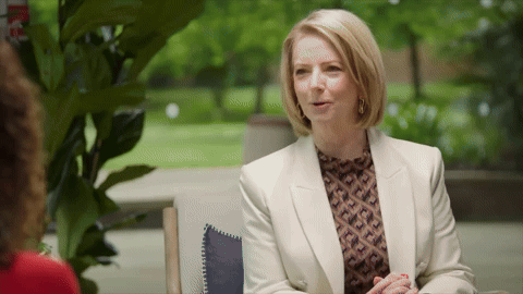 A middle-aged woman with short blonde hair sitting at a table outdoors, engaged in conversation.