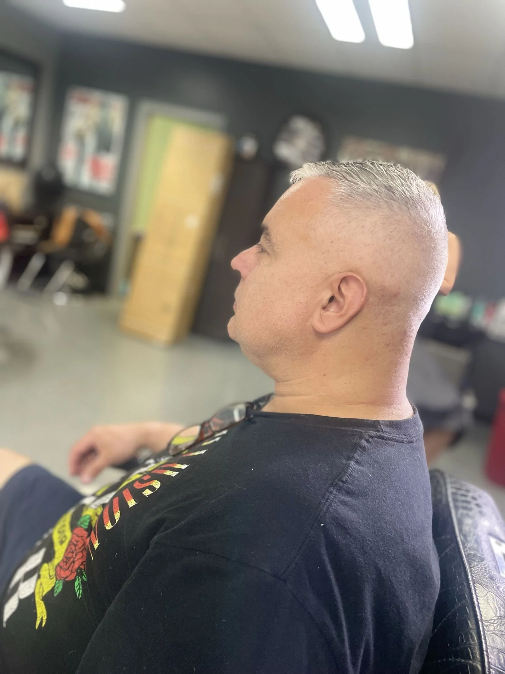 Side profile of a man with a crew cut hairstyle sitting in a barbershop chair.