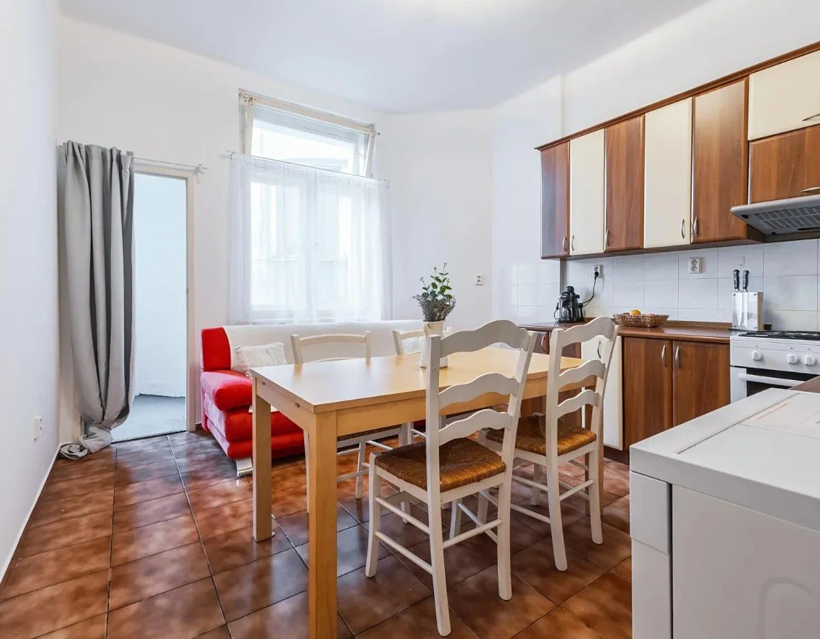Kitchen with a dining table, chairs, and a red couch near a window, with brown tile flooring and wooden cabinets.
