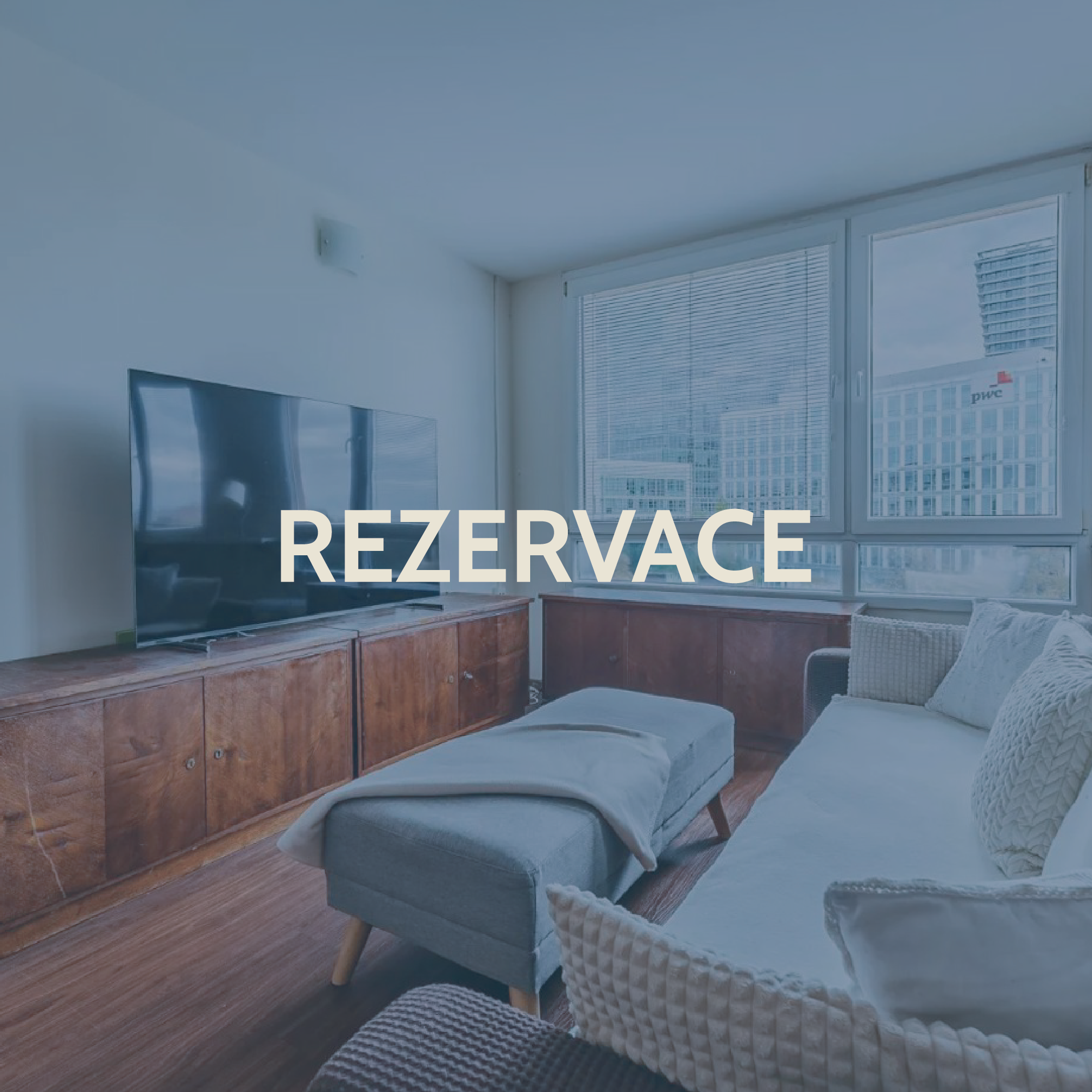 Living room with a large window, flat-screen TV on a wooden cabinet, sofa, and ottoman, with the word 'Rezervace' overlaid.