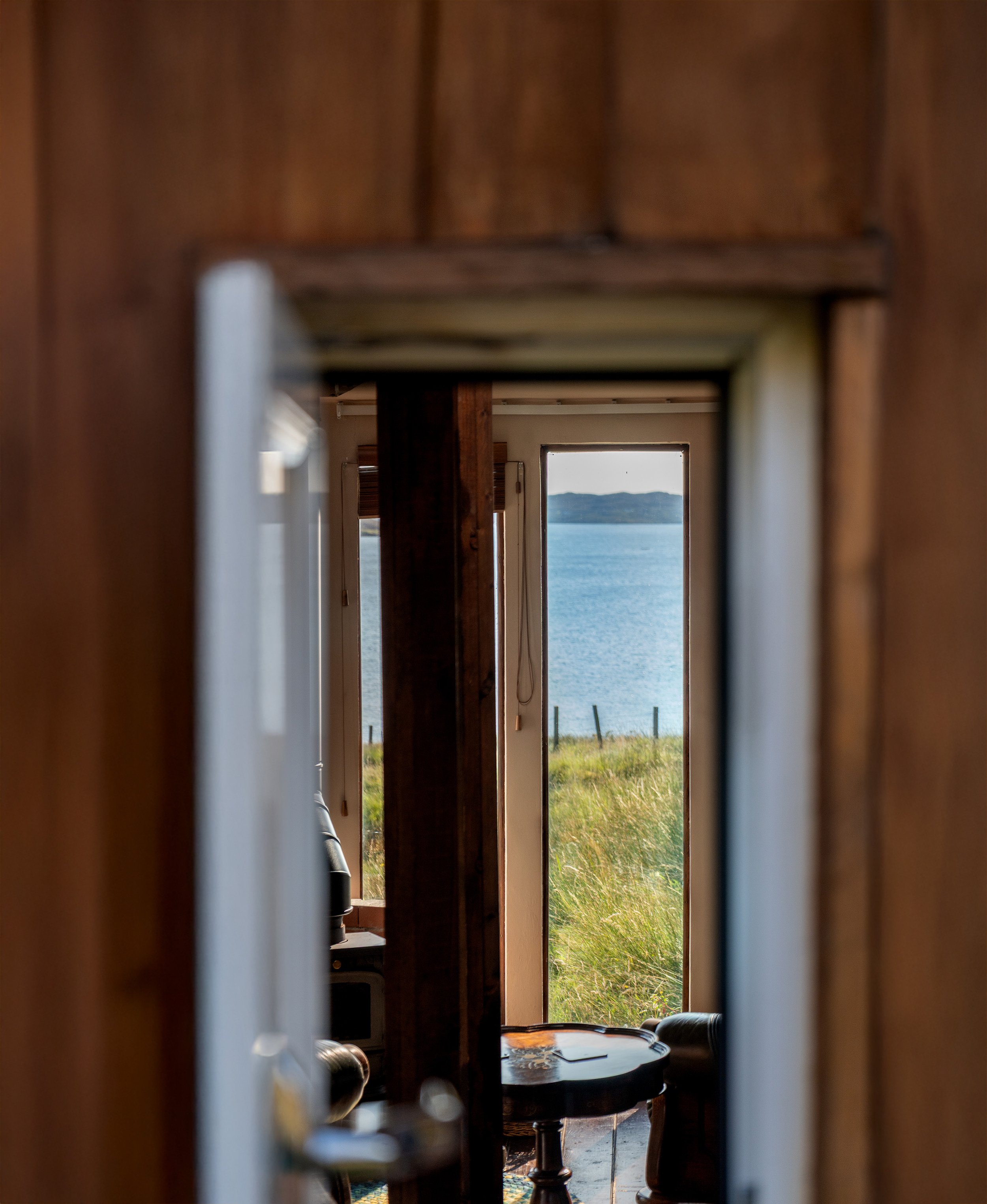 View of a beach and water seen through a window, framed by a narrow passage inside a wooden building.