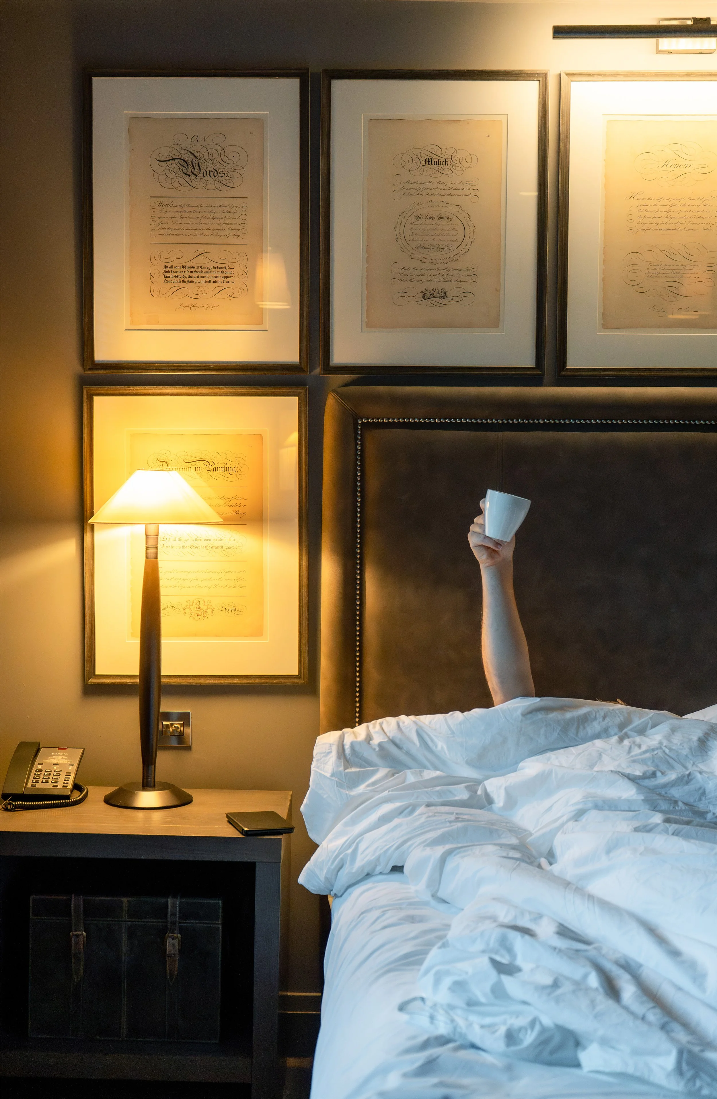 Person relaxing in a luxury hotel bed with a mug, showcasing comfort and hospitality