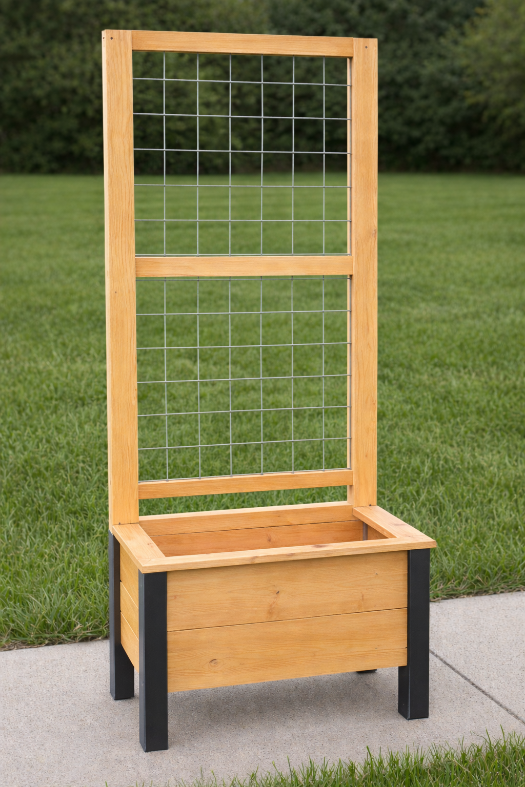 A wooden garden planter with a trellis on a sidewalk, green grass and trees in the background.