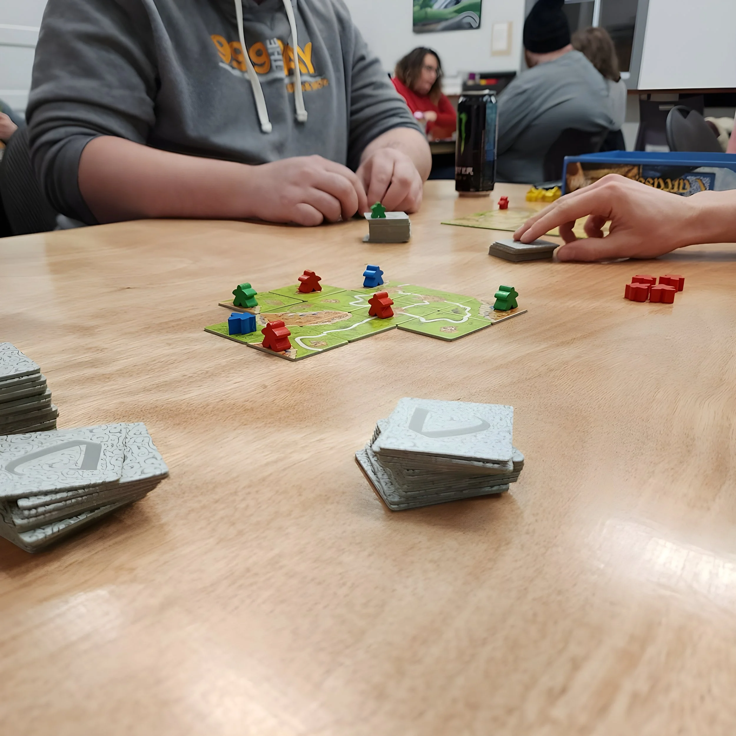 People playing the board game Catan at a table with game pieces and cards.