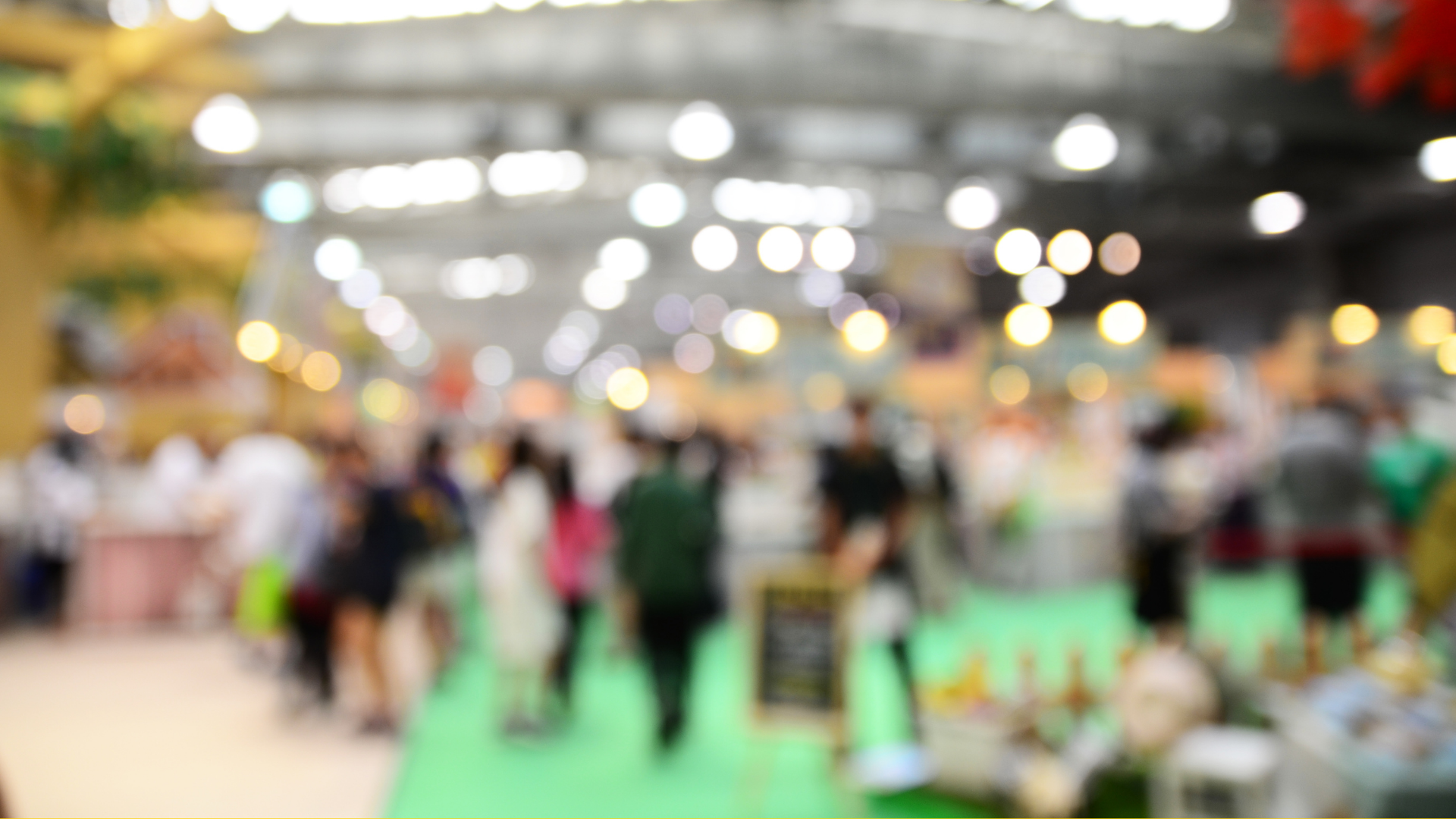 Blurred image of an indoor marketplace with people walking around and bright lights overhead.