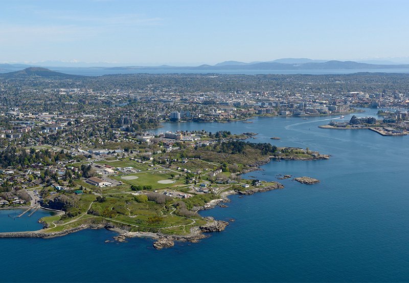 Aerial view of Esquimalt peninsula British Columbia, Canada. with green spaces, a few building and  surrounded by the pacific with mountains in the background.