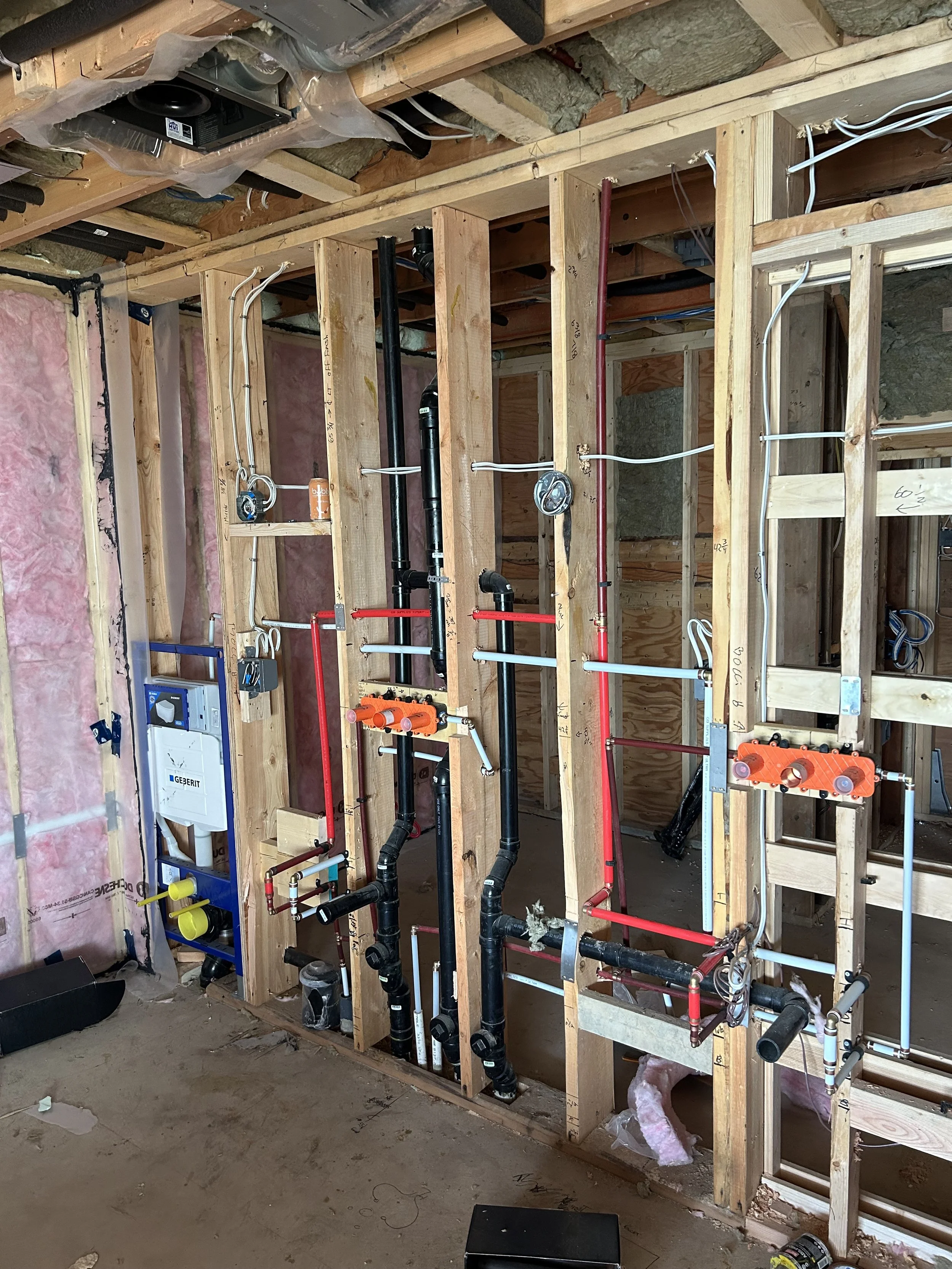 Construction site showing plumbing and electrical wiring installed in wooden framing of interior wall.