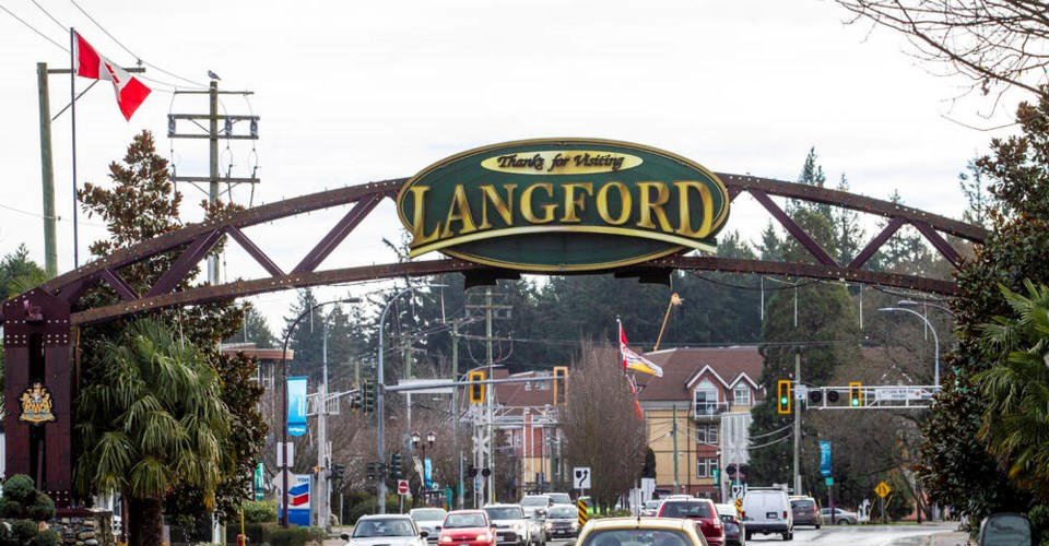 Entrance to Langford with a large sign saying "Thanks for Visiting Langford" on a metal arch, surrounded by trees, buildings, cars, traffic lights, and flags.
