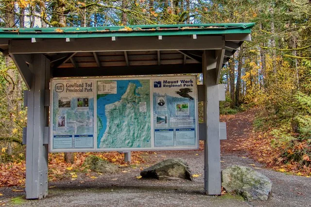 Information board at Gowlland Tod Provincial Park, Mount Work Regional Park, with a map and park details, surrounded by trees in a forest setting.